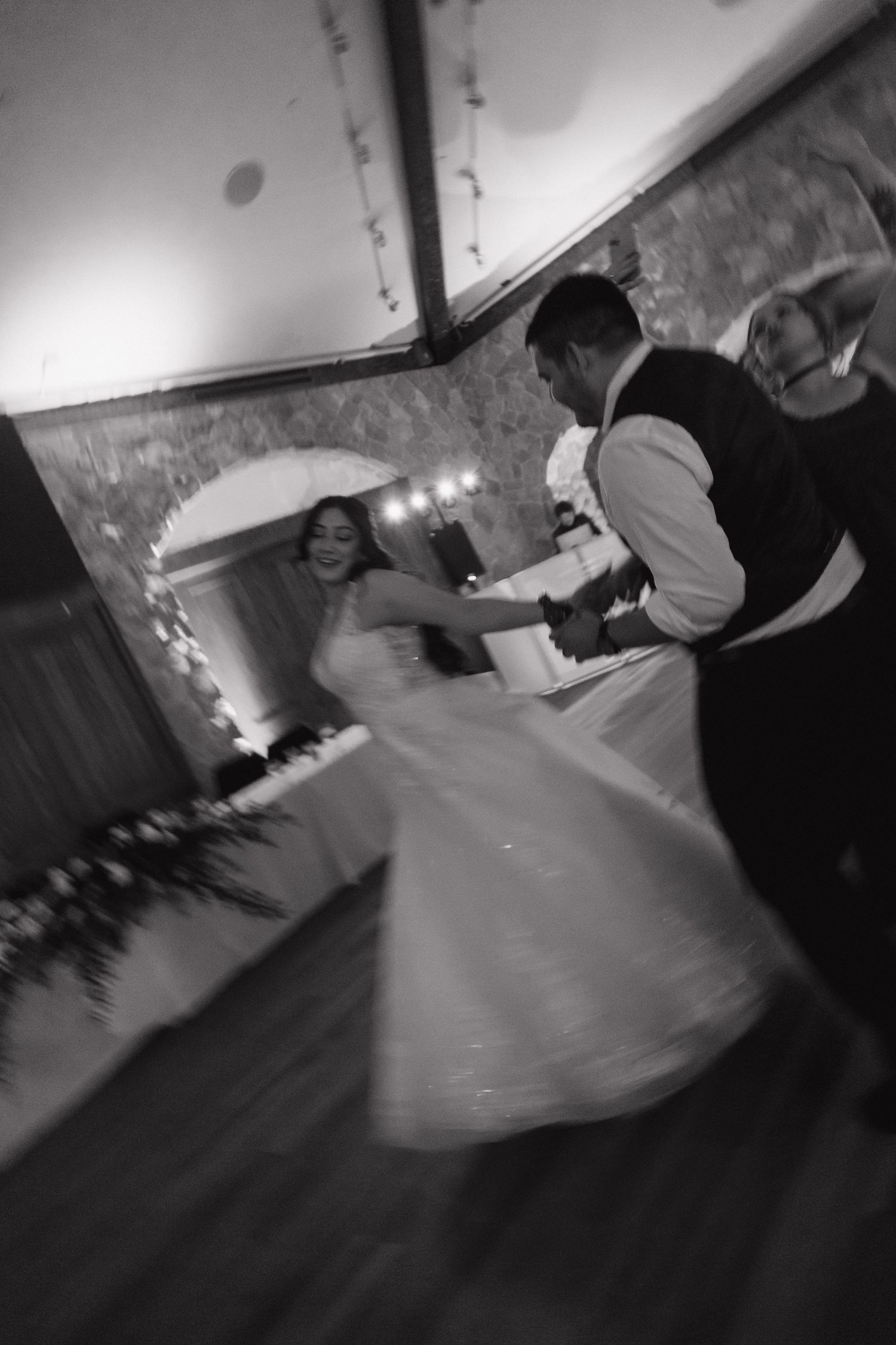 Bride and groom spin joyfully on dance floor in blurred motion black and white wedding photo.