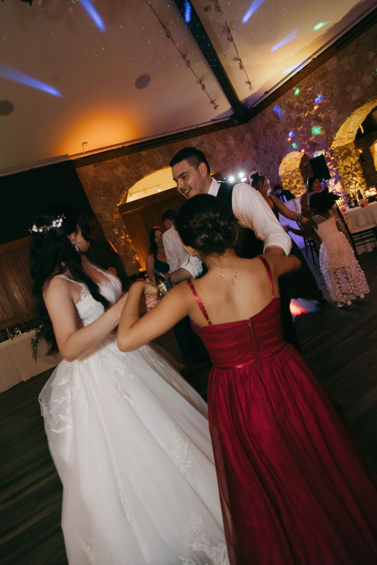 Bride and groom dancing with bridesmaid in red dress at wedding reception.