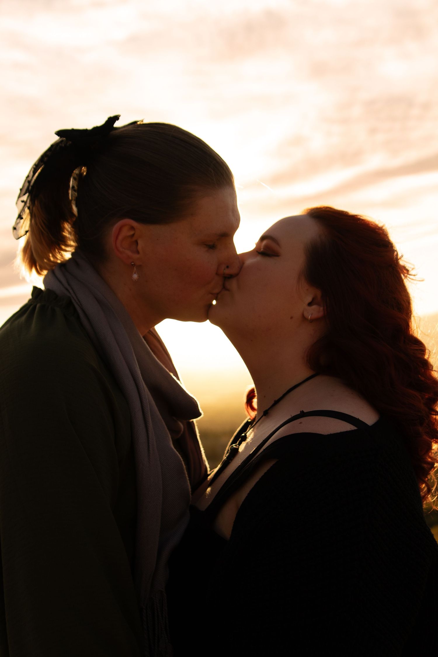 Two women sharing a romantic kiss silhouetted against a golden sunset sky.