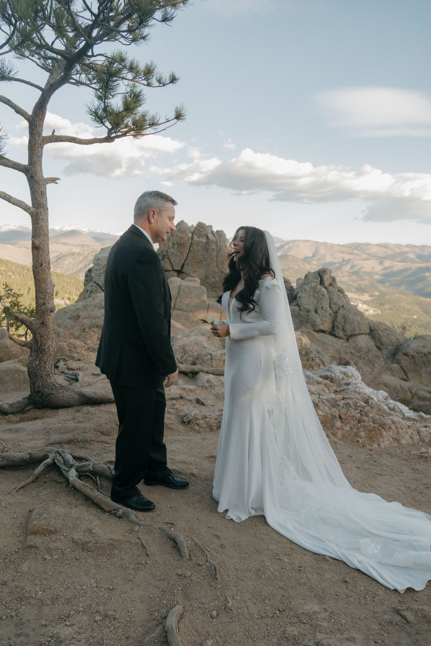 A bride and groom exchange vows on a rocky mountain overlook with sweeping landscape views behind them.