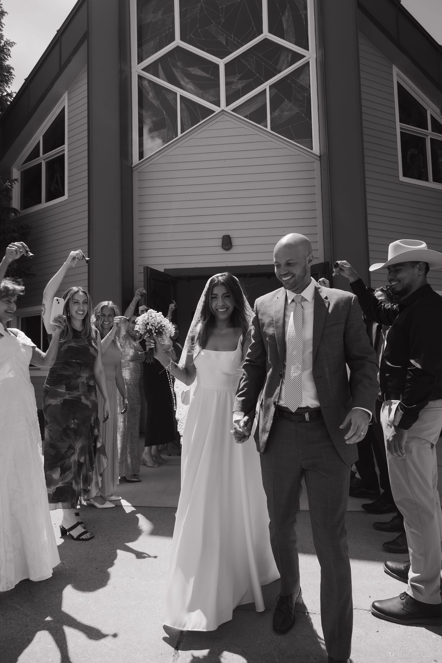 Black and white photo of newlyweds exiting church as guests celebrate their wedding ceremony.