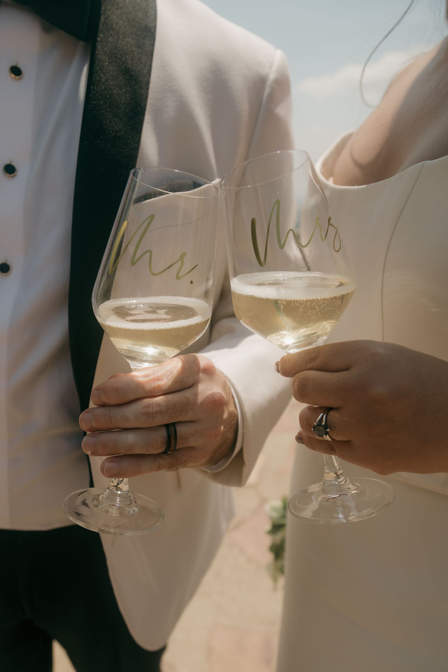 Newlyweds toasting with Mr. and Mrs. champagne glasses at sunny outdoor wedding celebration.
