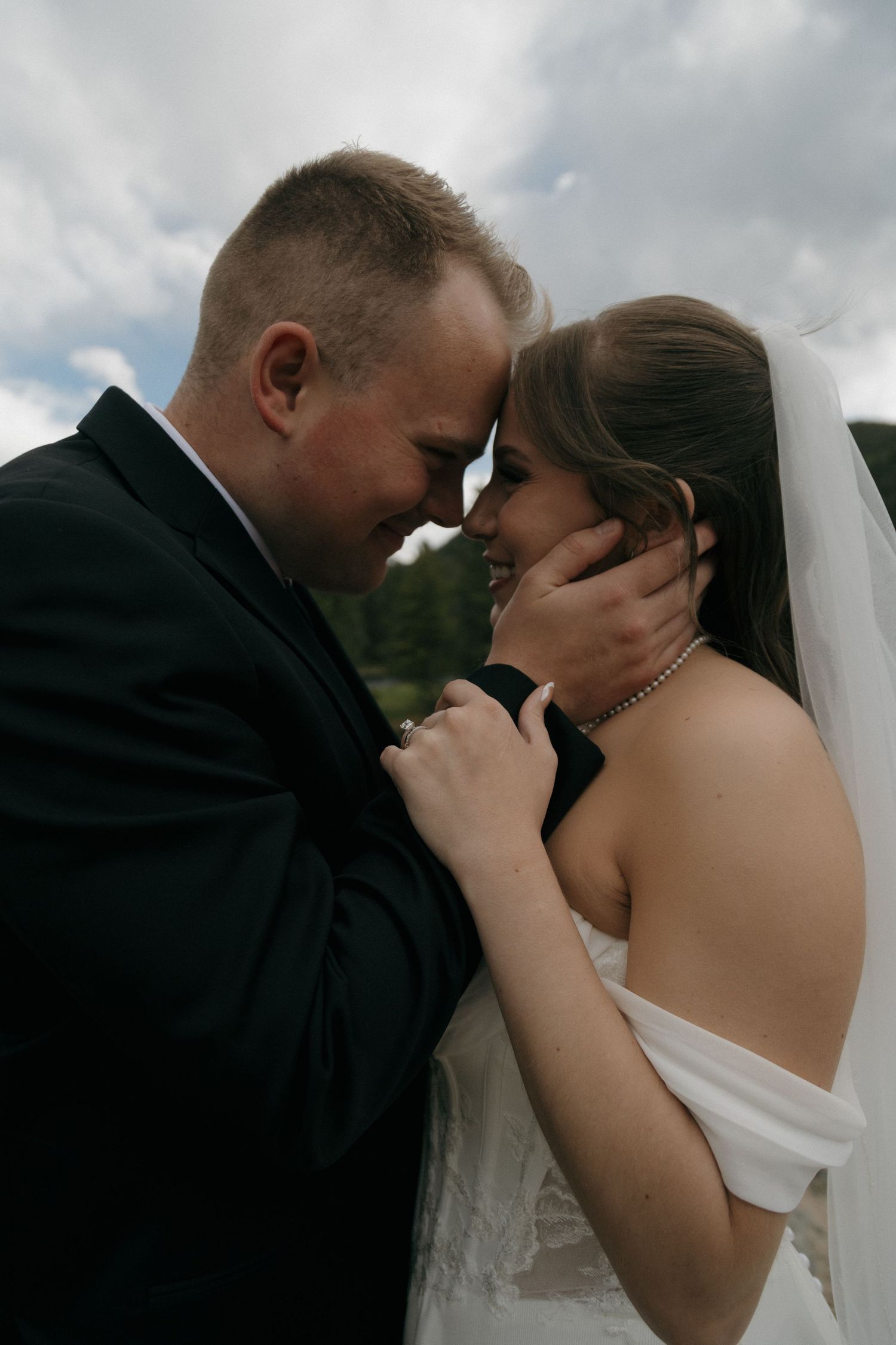 Bride and groom share romantic forehead touch moment on their wedding day outdoors.