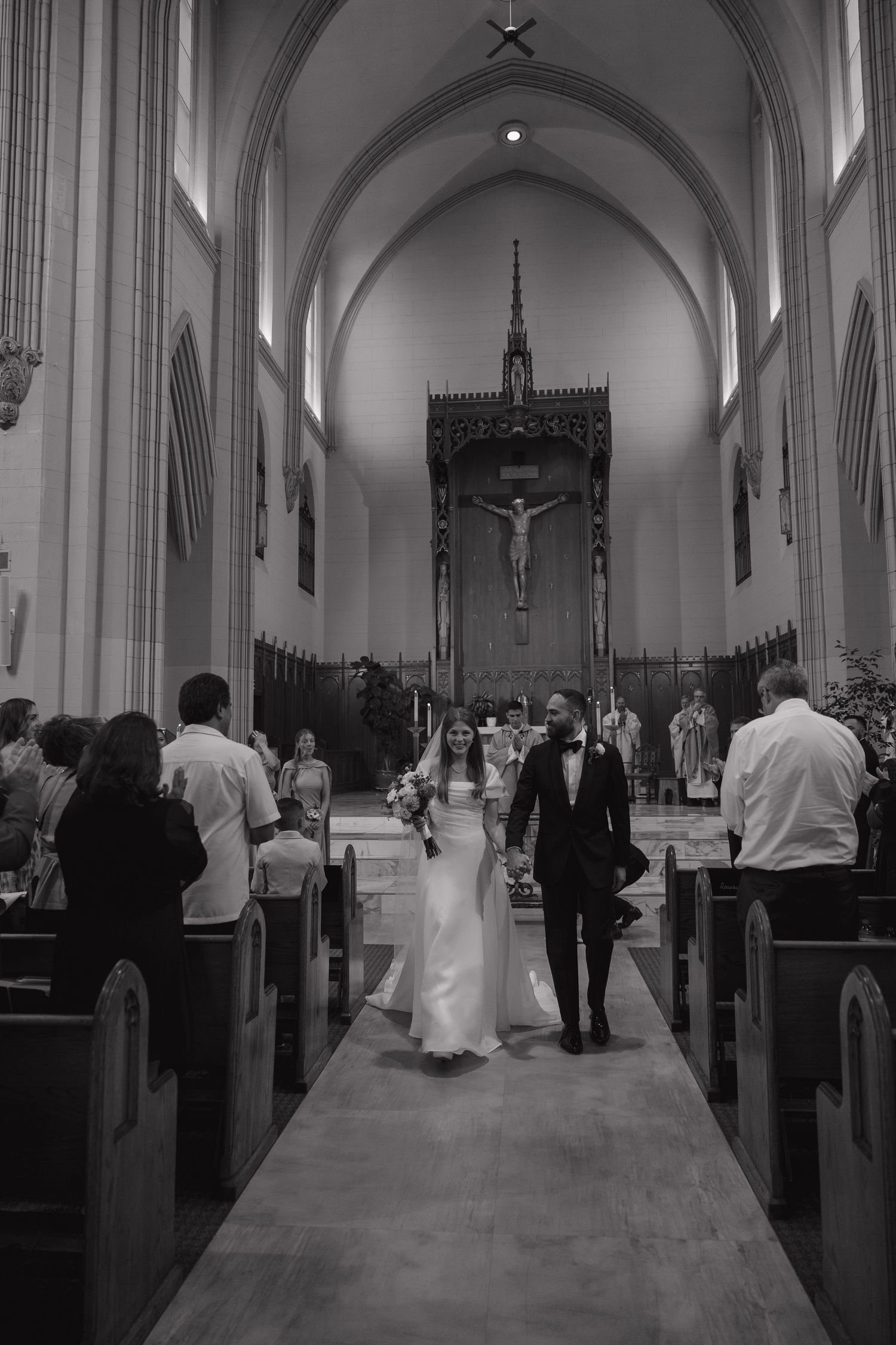 Black and white photo of bride and groom walking down cathedral aisle after ceremony.