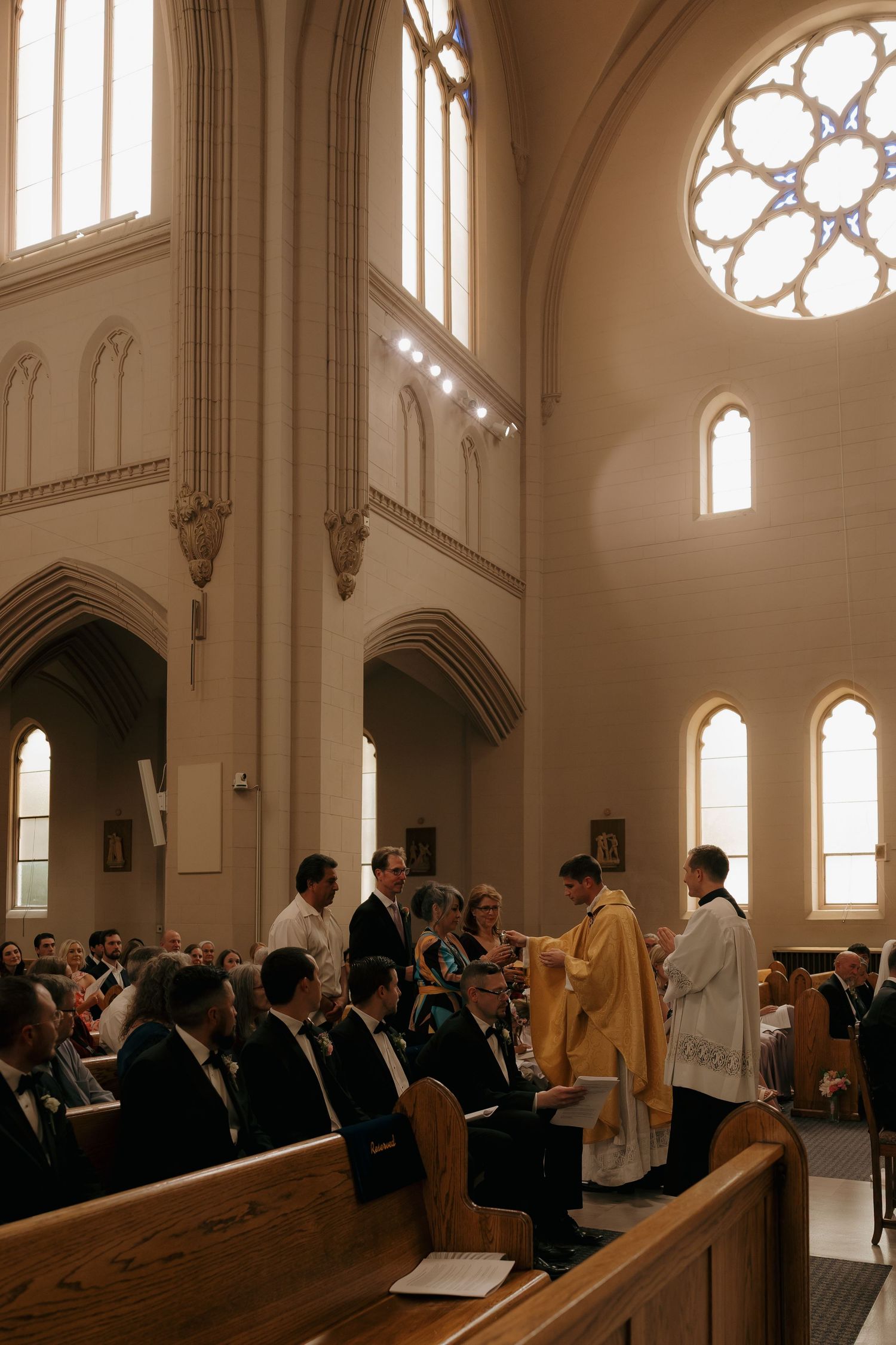 Priest in golden vestments officiating a Catholic wedding ceremony inside an elegant church with arched windows.