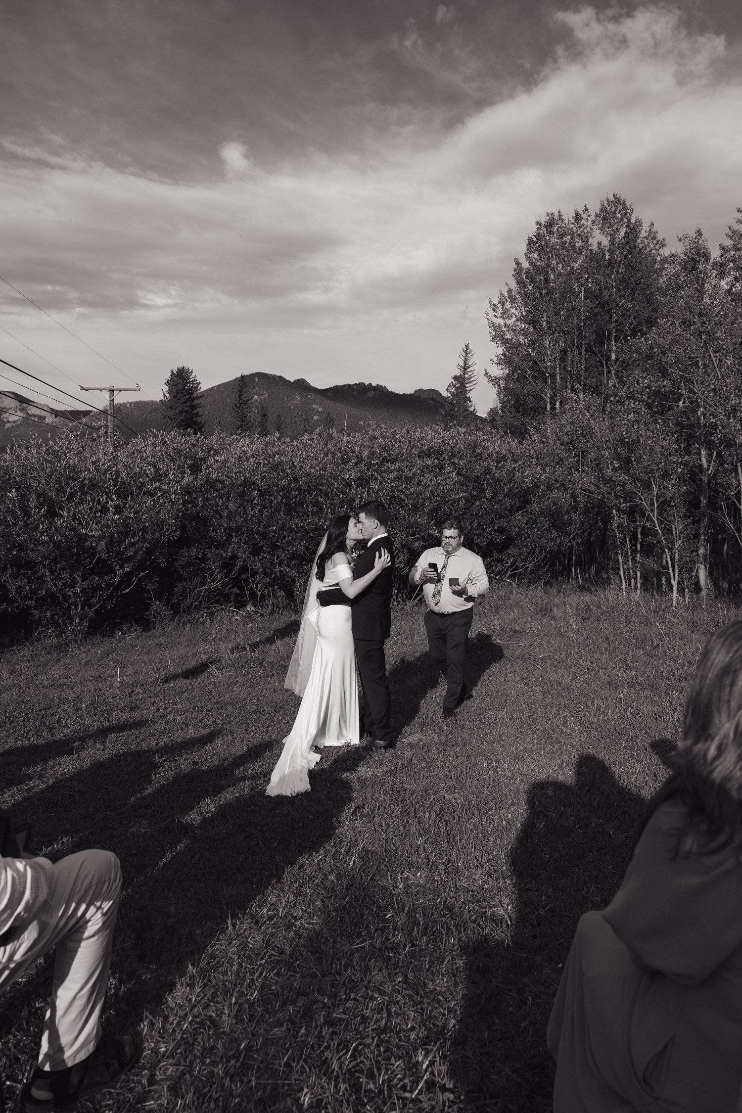 Black and white photo of a bride and groom sharing their first dance outdoors on a grassy field during a rustic wedding ceremony.
