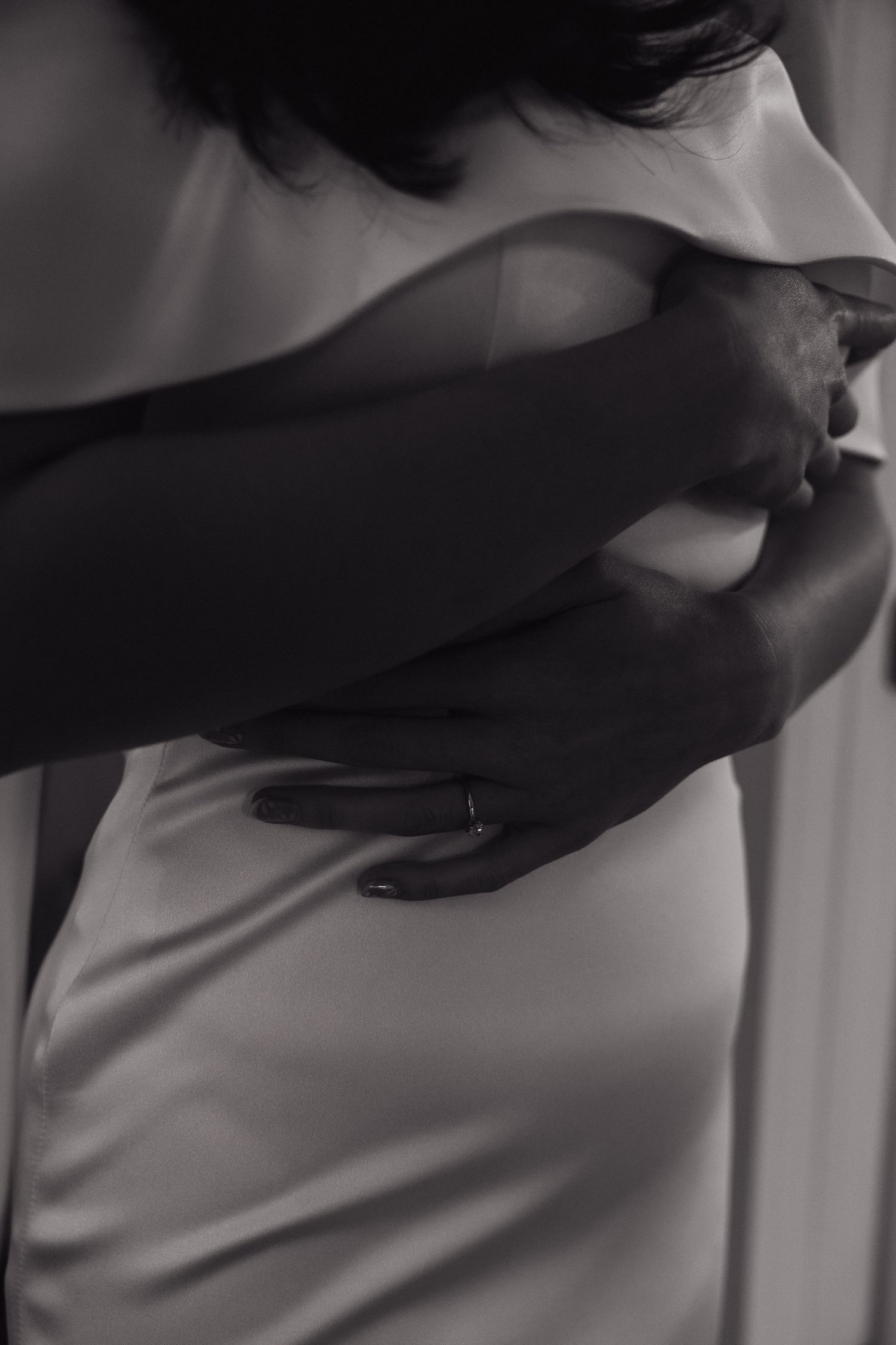 Black and white photo of a groom embracing a bride in a white satin wedding dress.