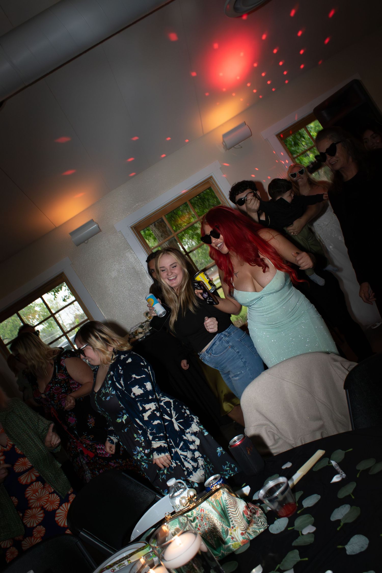 People dancing and mingling at an indoor celebration with red lighting effects.