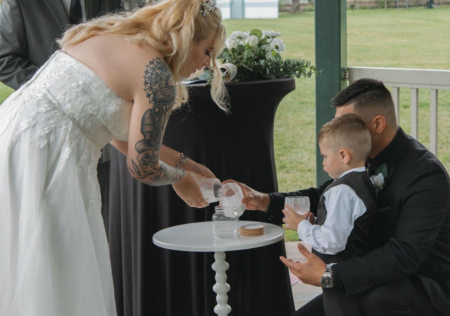 Wedding participants gather around a decorative table during an outdoor ceremony.
