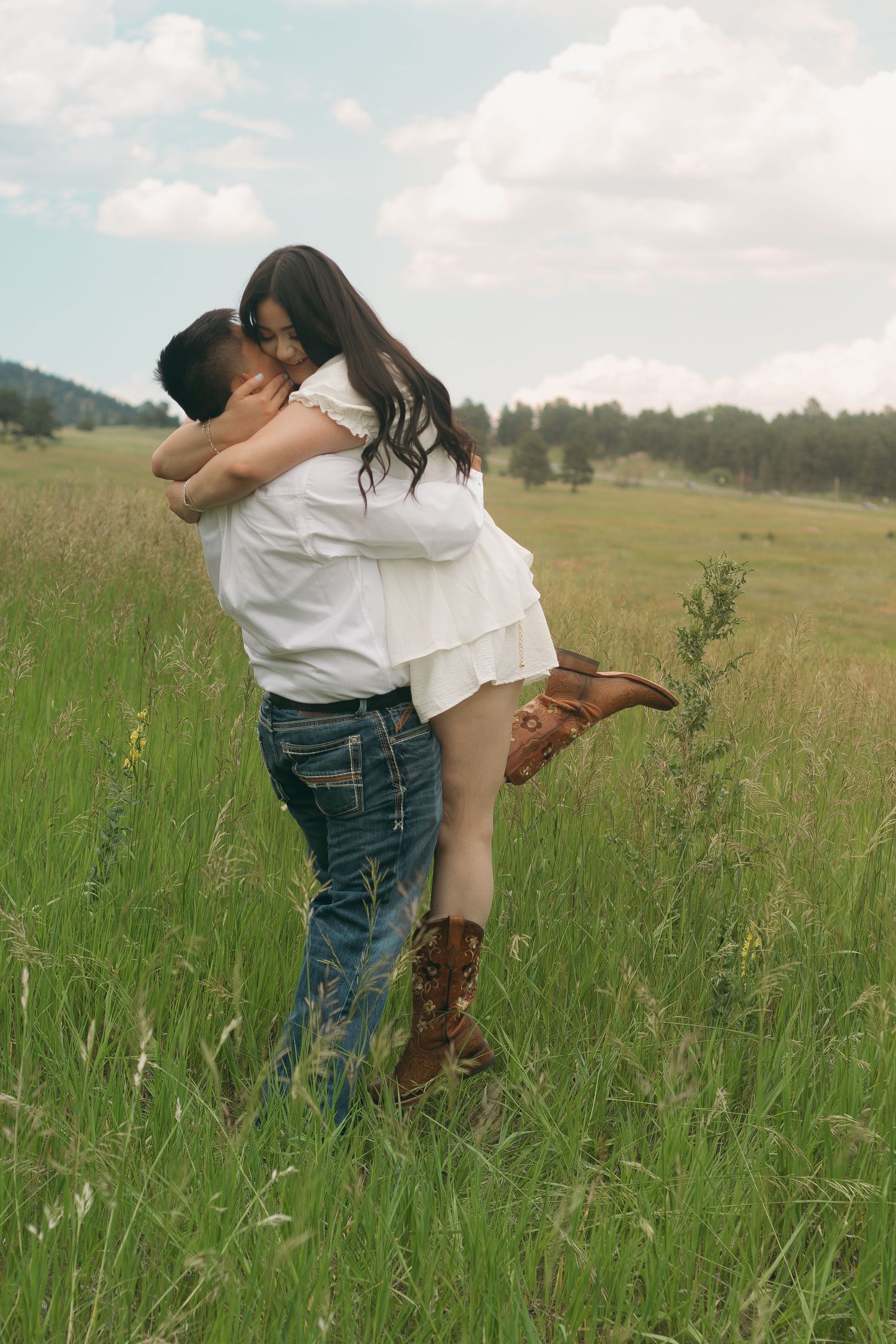 Playful lift in mountain meadow with cowboy boots and white summer outfits.