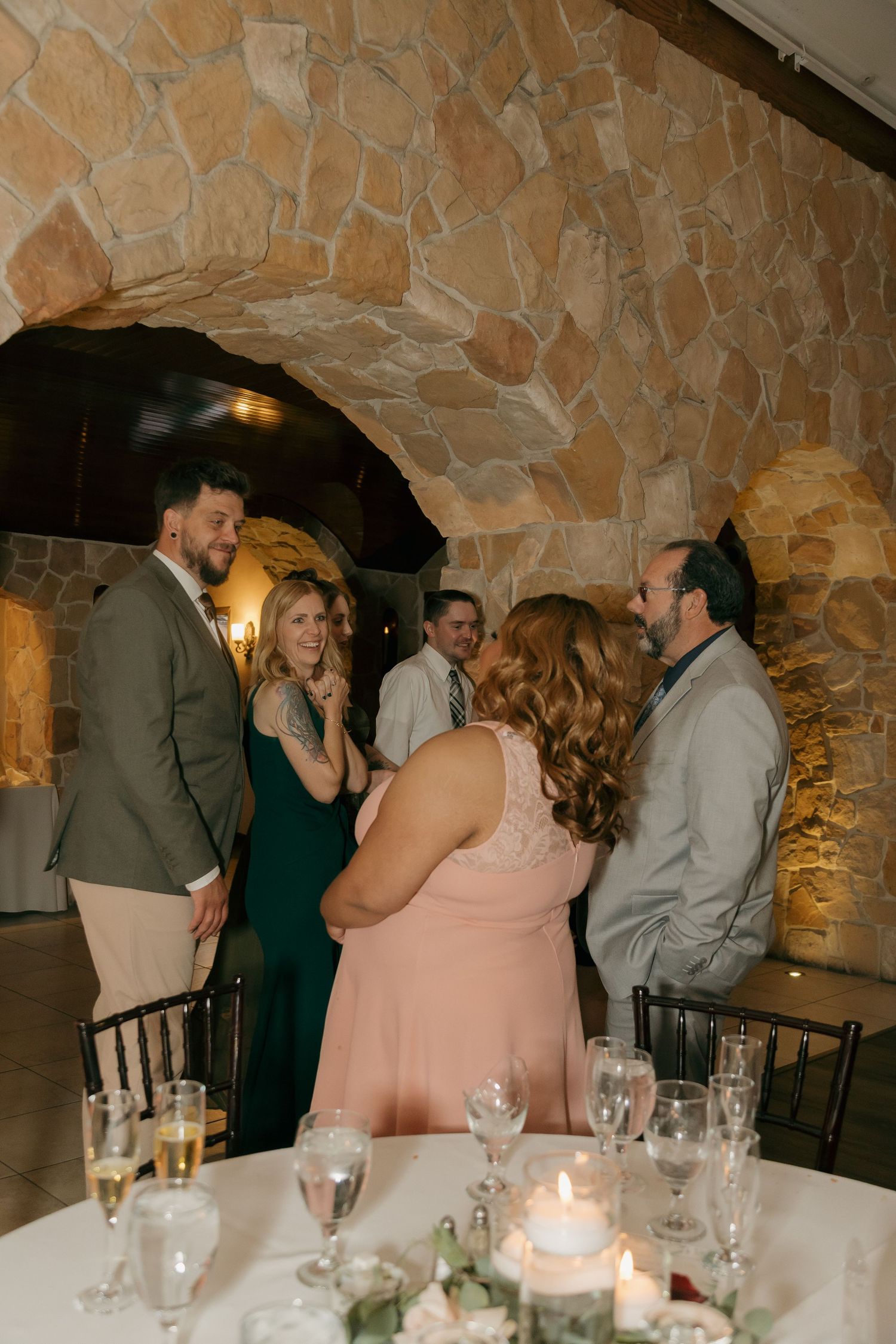 Wedding guests mingling and conversing at reception table in stone arch venue.