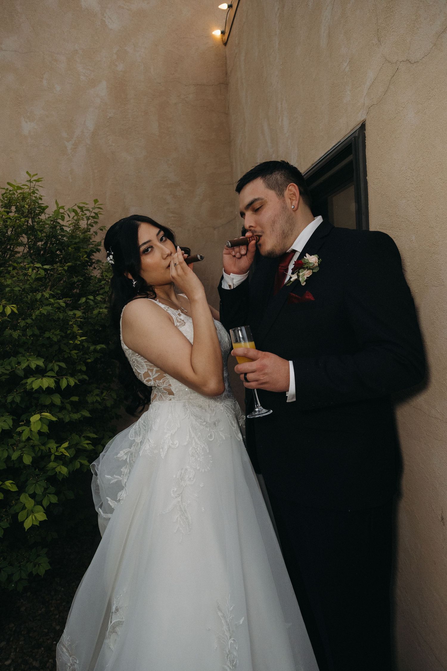 Bride and groom enjoy cigars and champagne together in a romantic outdoor setting at their wedding reception.