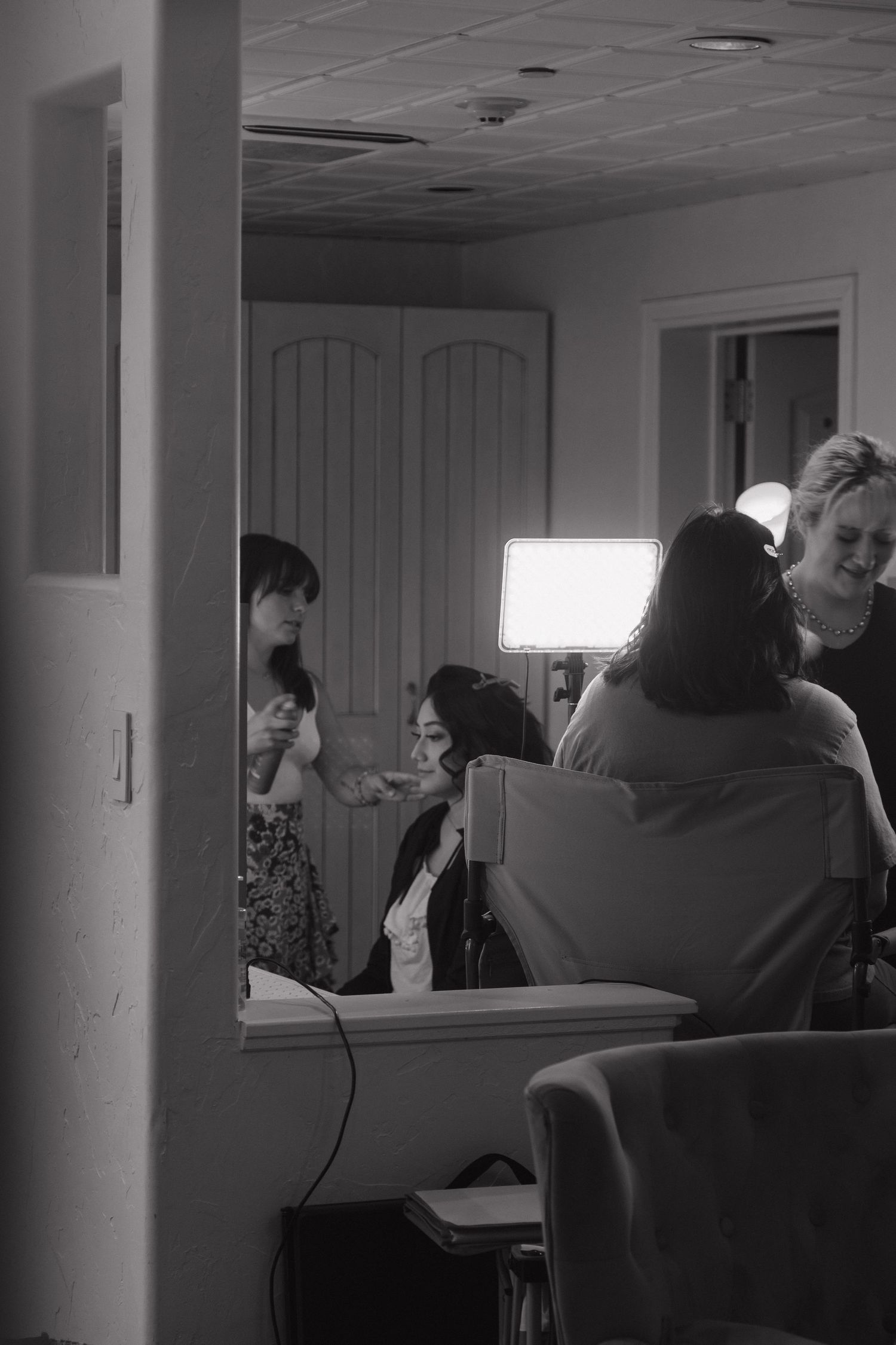 Black and white photo of bridal party getting hair and makeup done in preparation room with bright studio lighting.