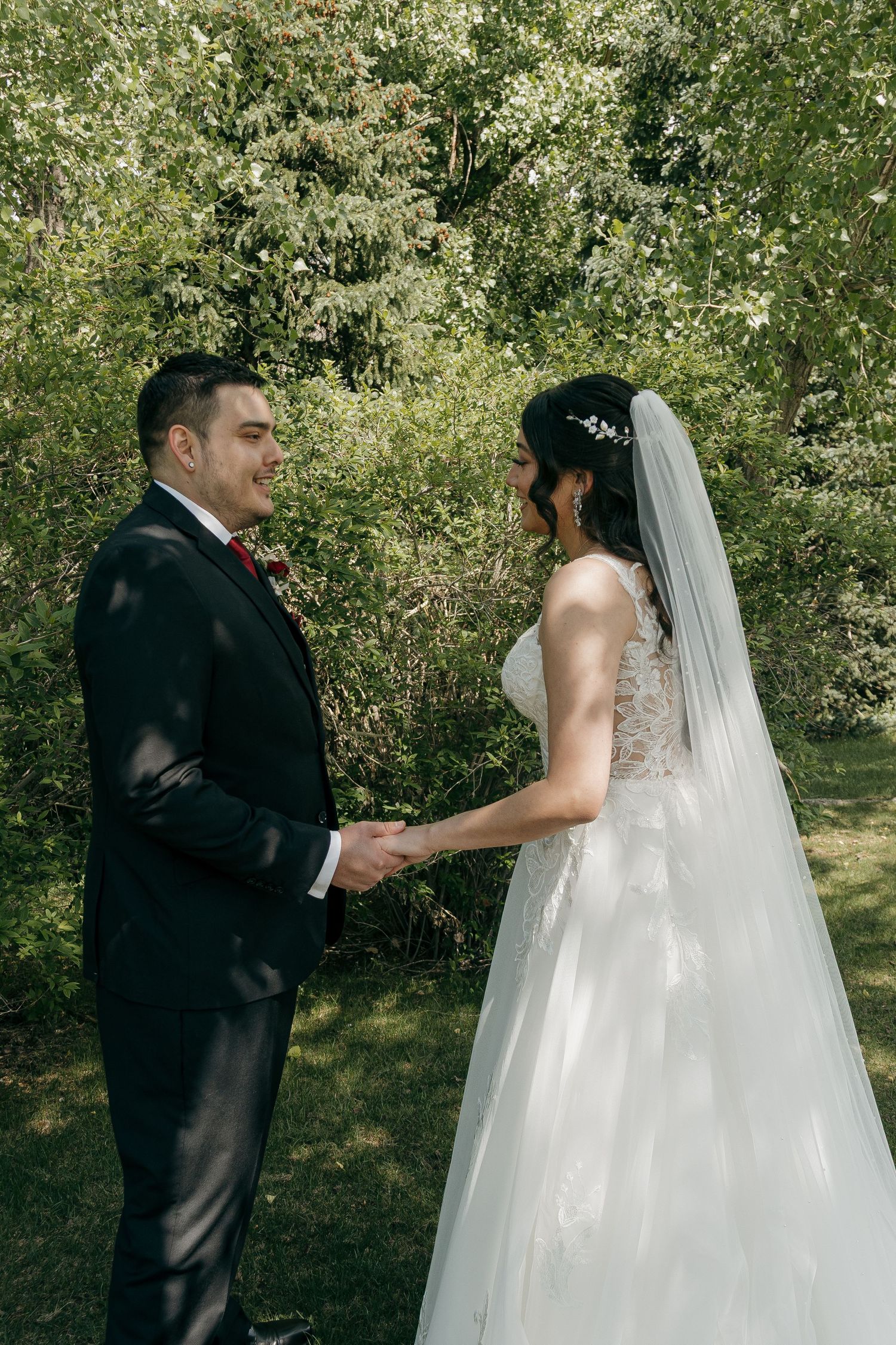Bride and groom sharing a first look moment holding hands in a lush green garden setting.