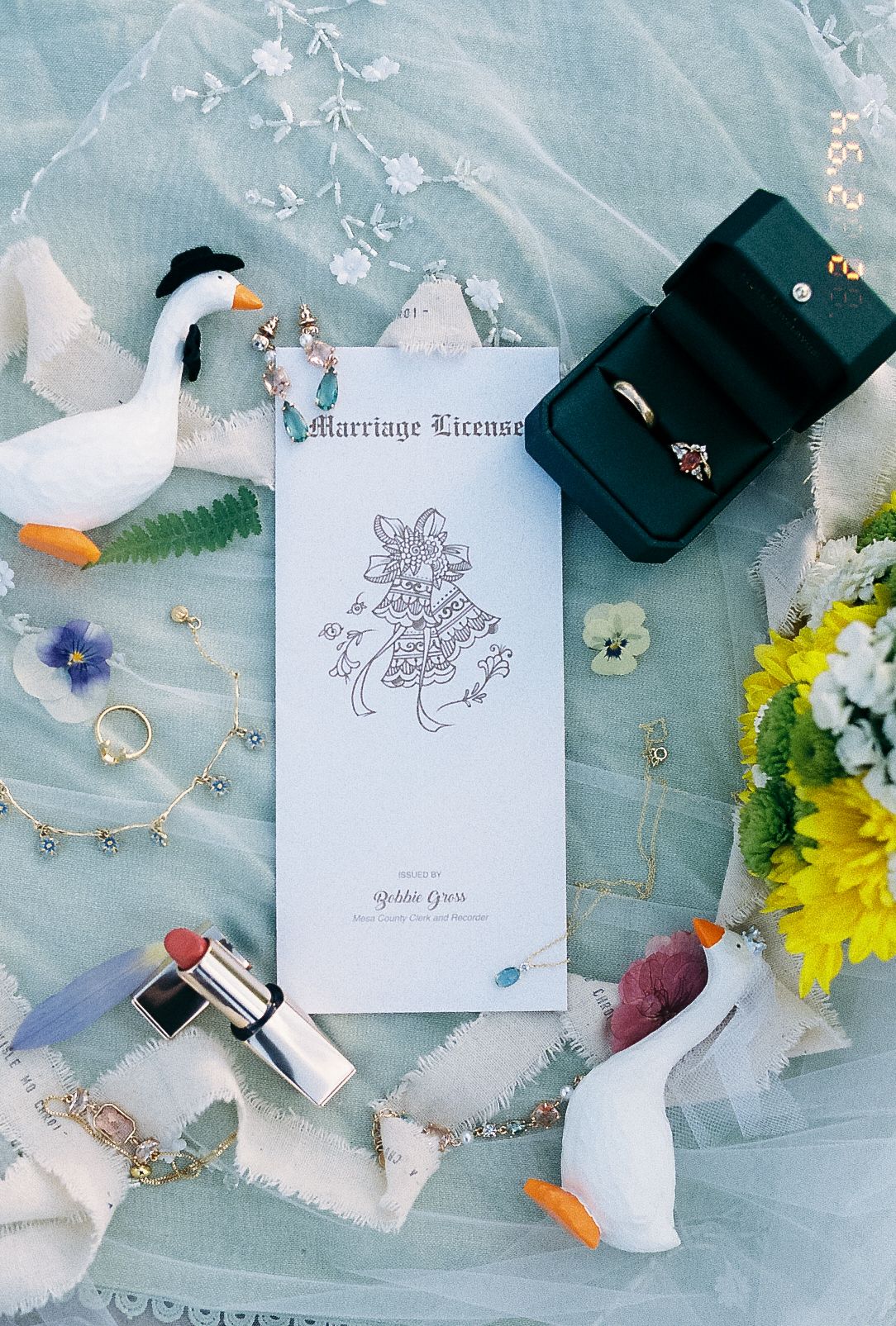 Flat lay of wedding details including marriage license, rings, duck toys, and yellow flowers.