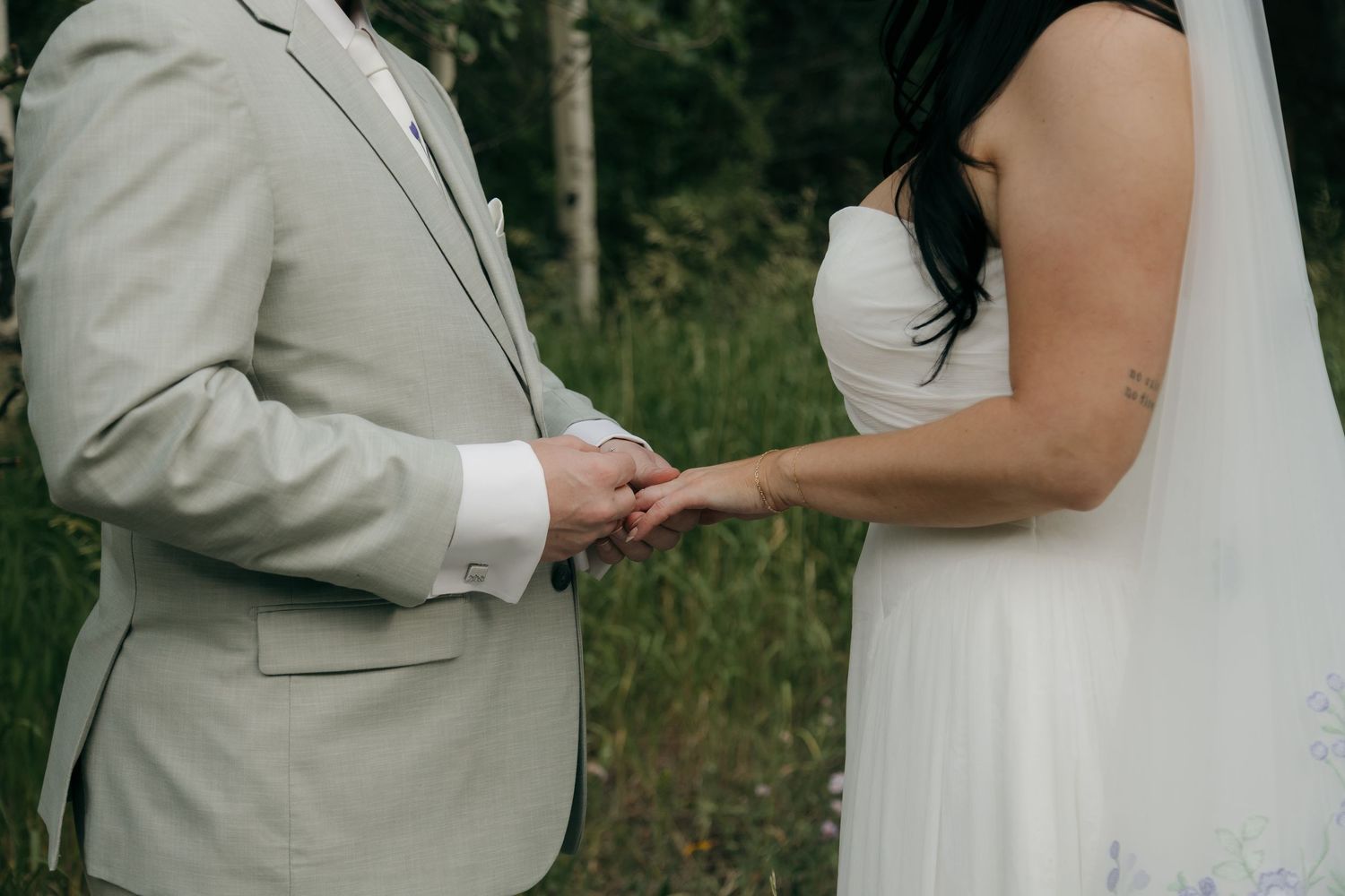 Bride and groom exchanging rings outdoors in a lush green forest setting during their wedding ceremony.