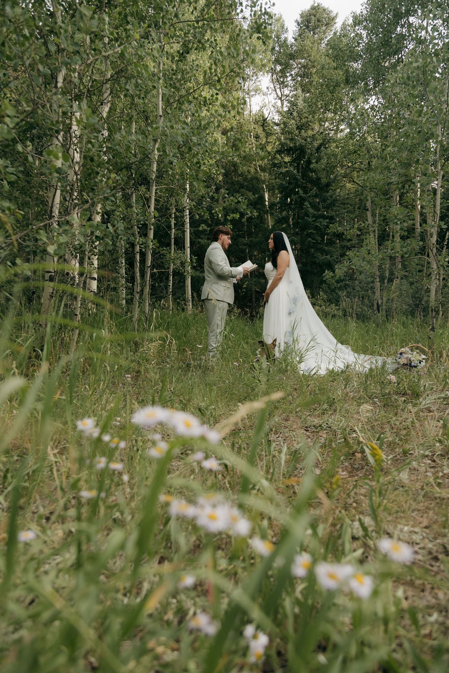 Bride and groom exchange vows in a sunlit forest meadow with wildflowers.
