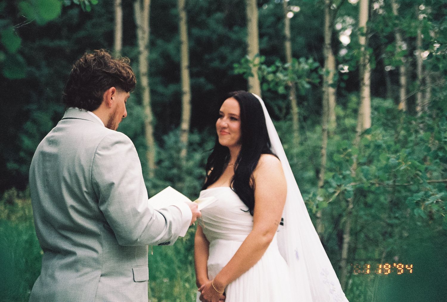 Bride and groom exchanging vows in a sunlit forest during an intimate outdoor wedding ceremony.