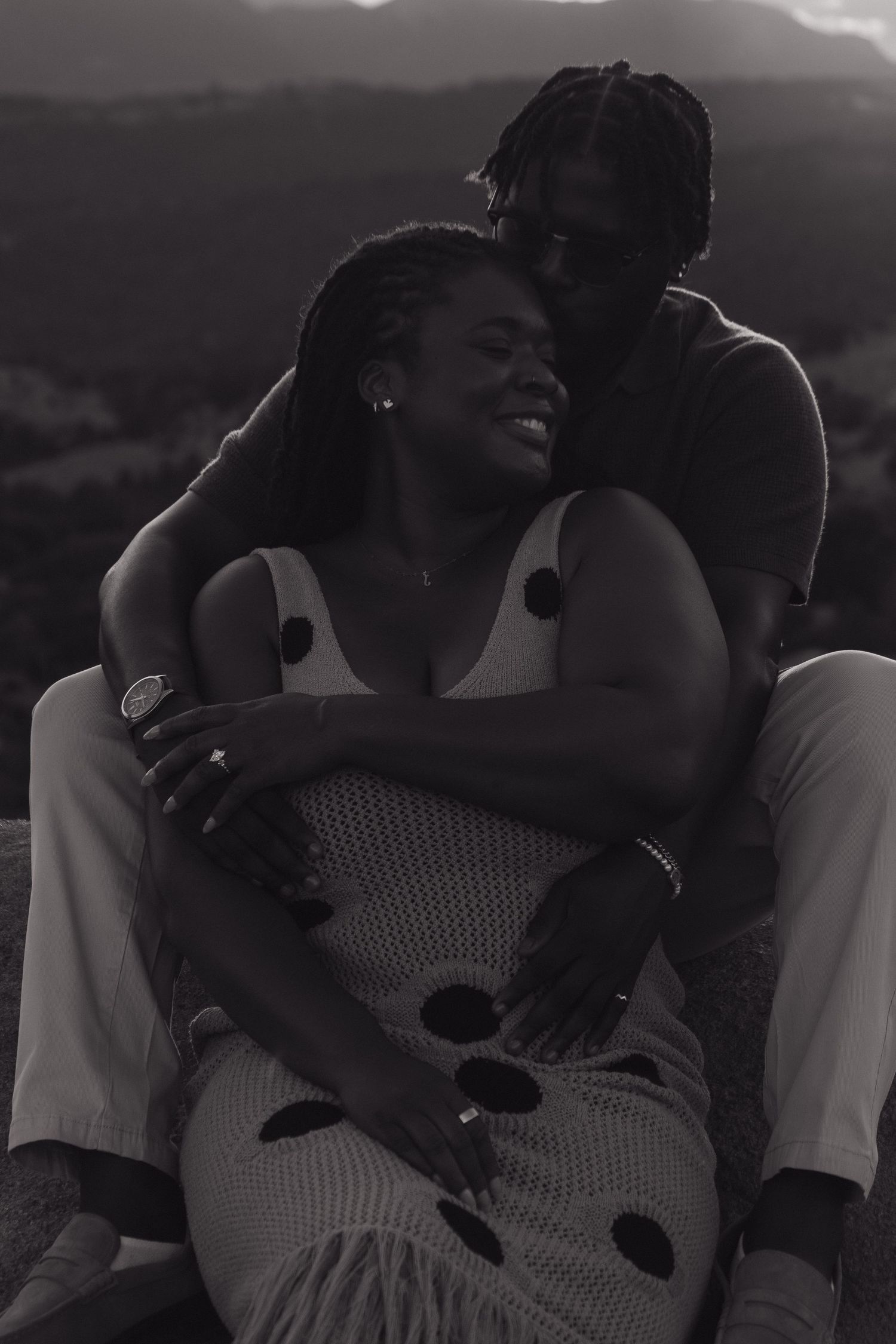 Silhouetted couple embracing at sunset with mountains in background.