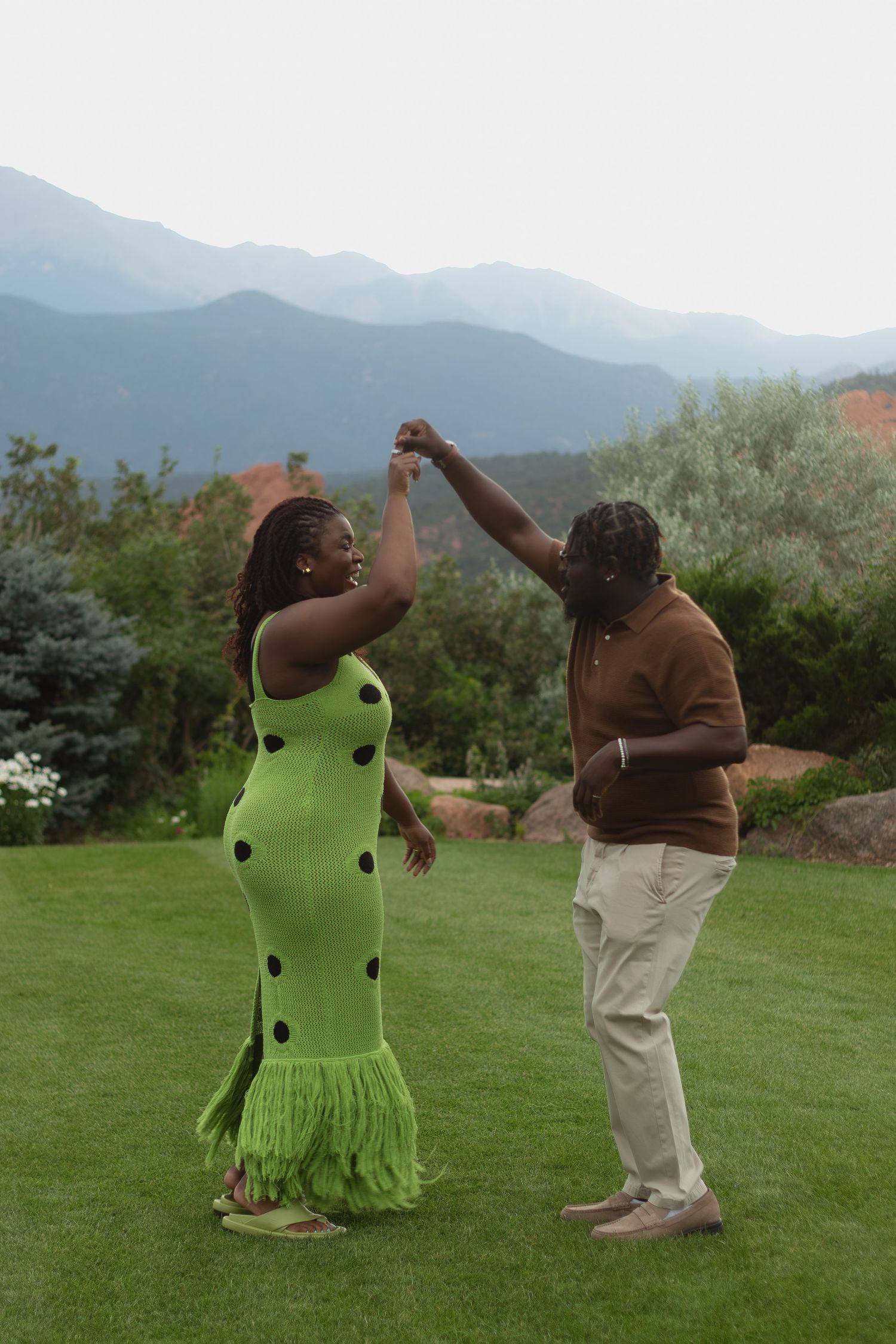 A couple dances together on a lawn with mountains in the background.