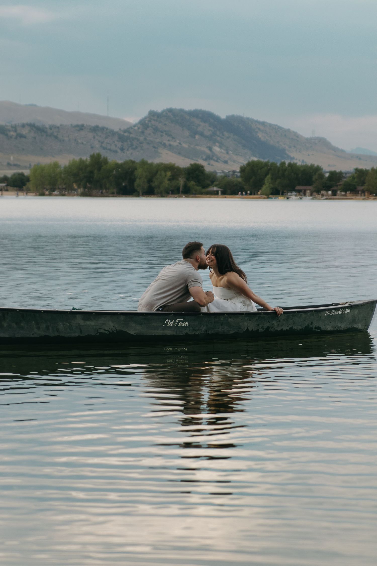 Two people lean close together while sitting in a canoe on a serene mountain lake.