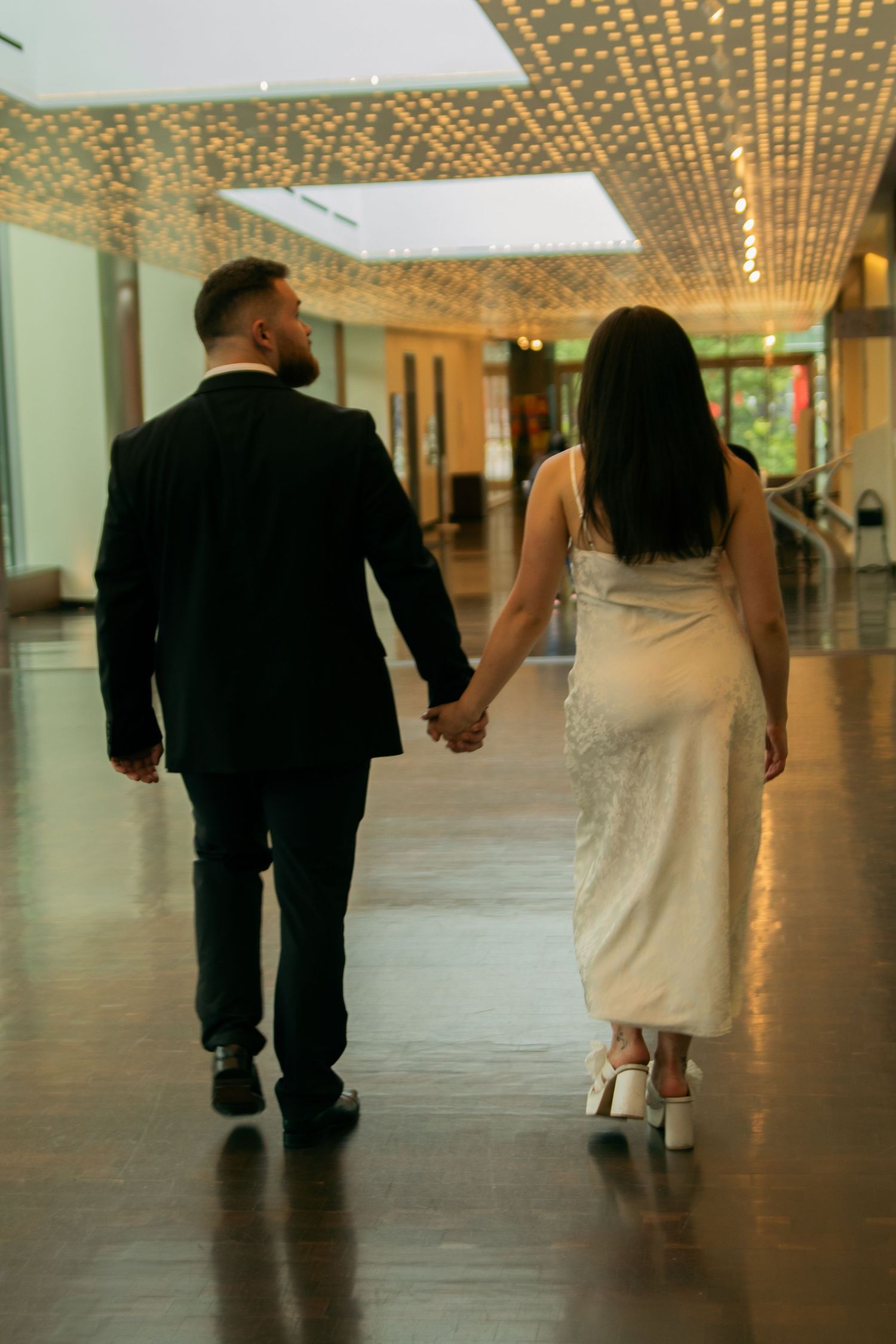 A couple walks through an elegant hallway with twinkling ceiling lights.