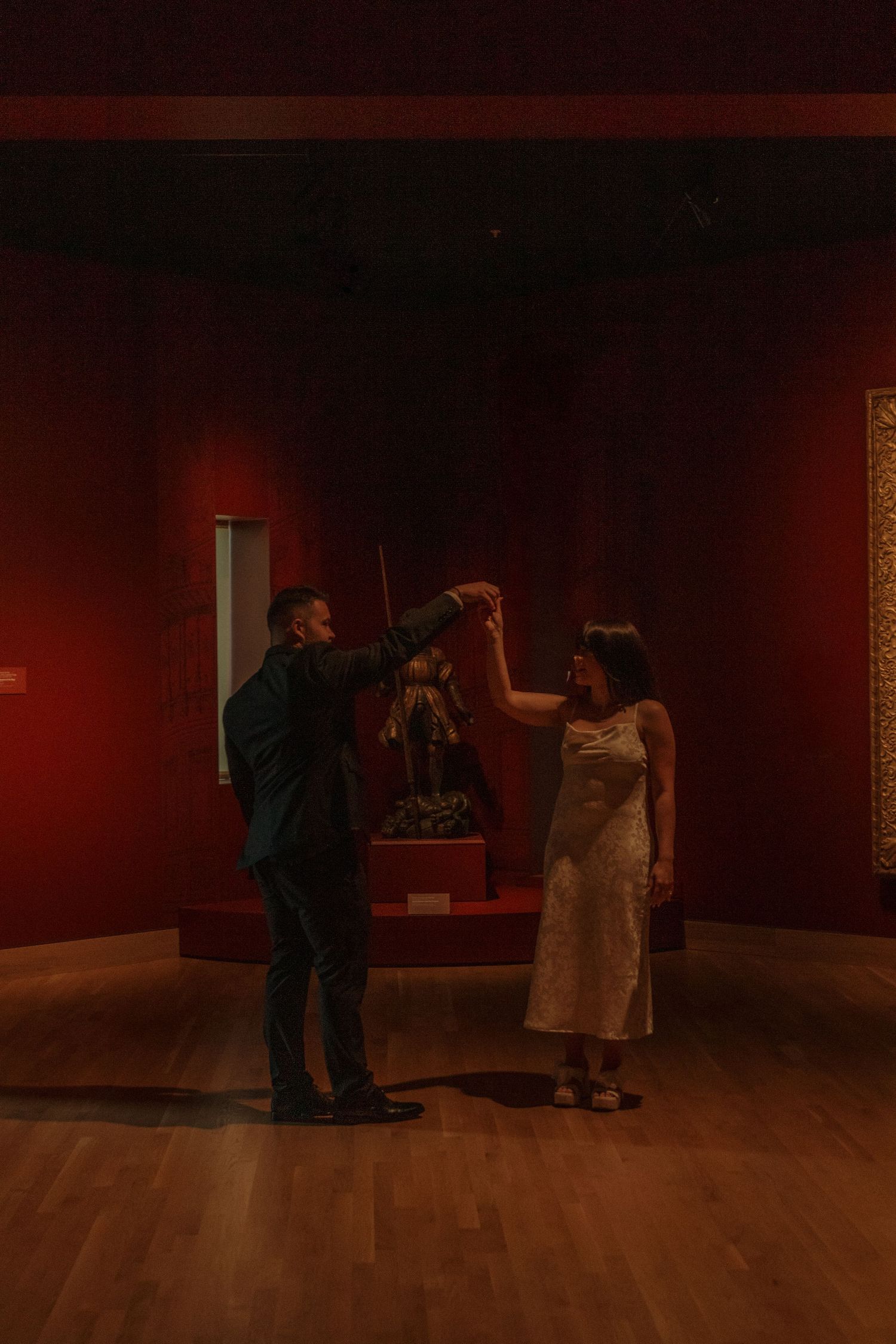 A couple dances together in an elegant art gallery space with deep red walls.