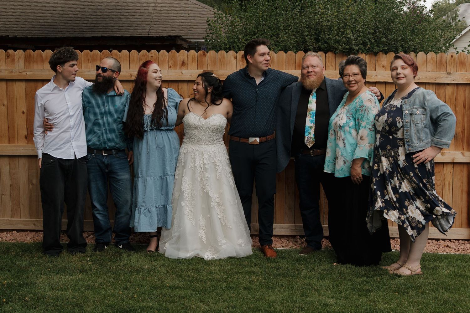 Guests gathering for an intimate backyard wedding celebration with natural greenery and wooden fencing.