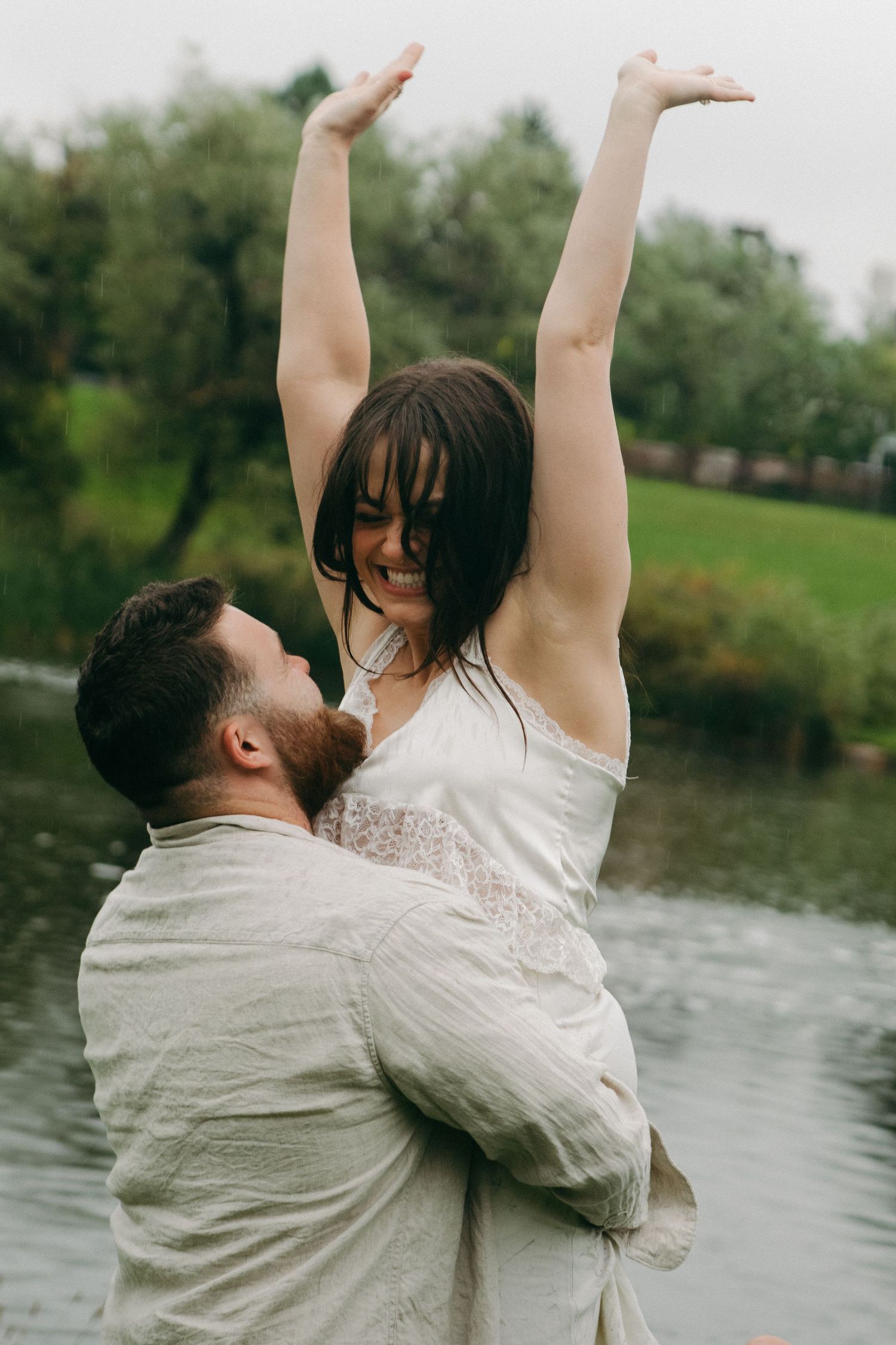 Couple embracing near a lake with raised arms in a moment of celebration.