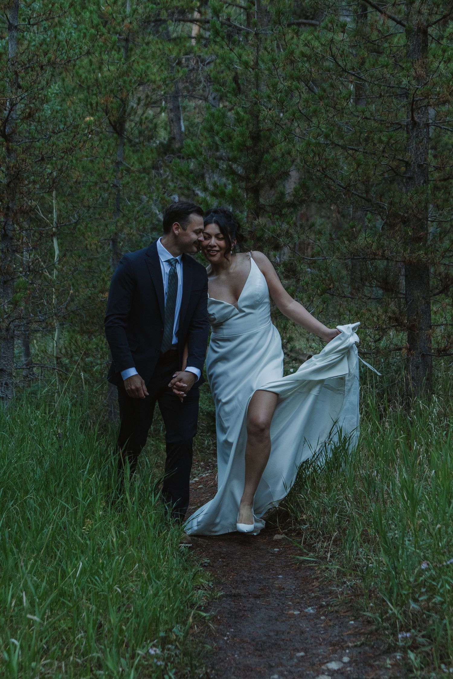 A couple shares an intimate moment on a trail surrounded by green forest.