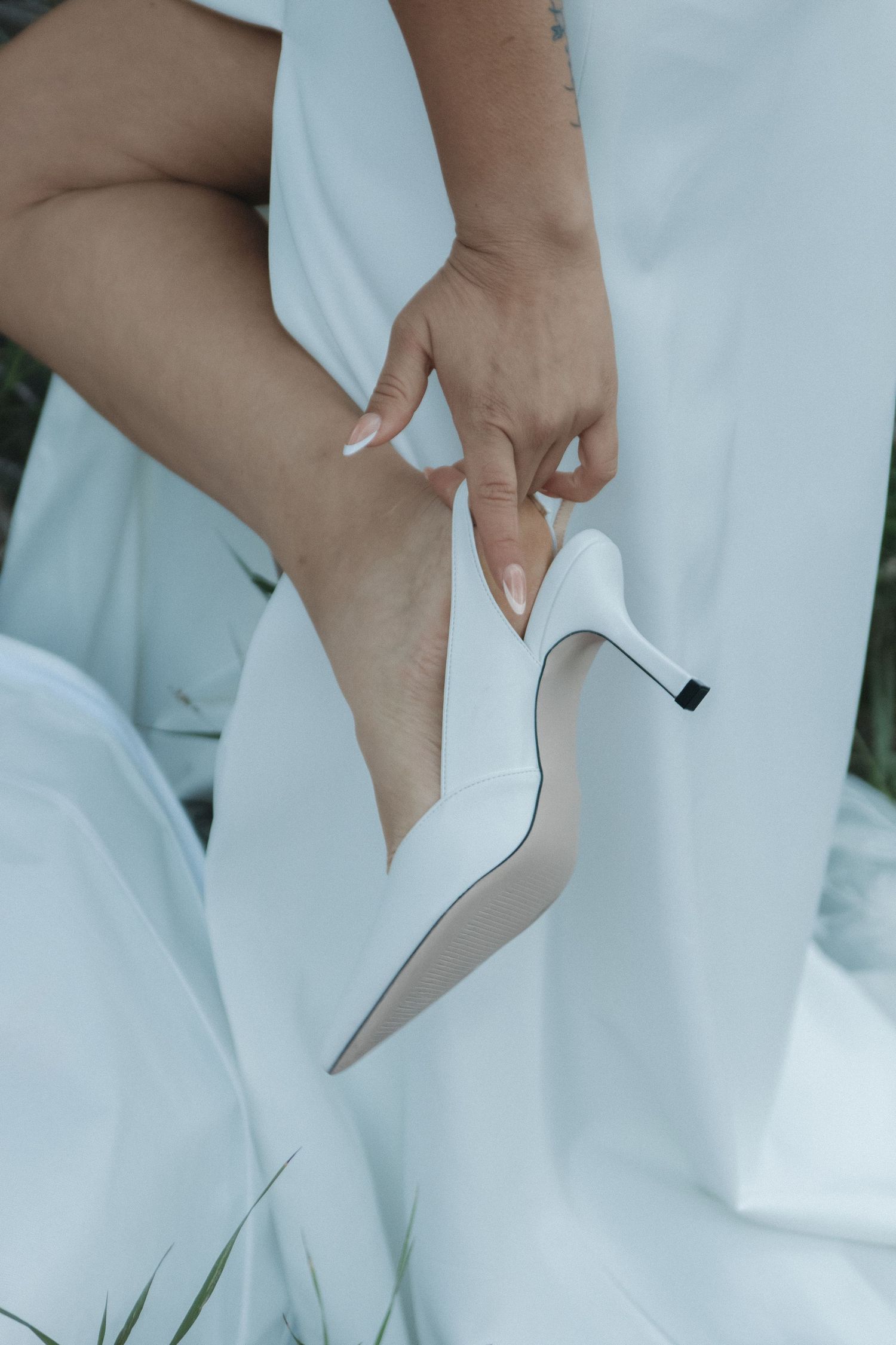 Close-up of a bride putting on elegant white wedding shoes against light fabric.