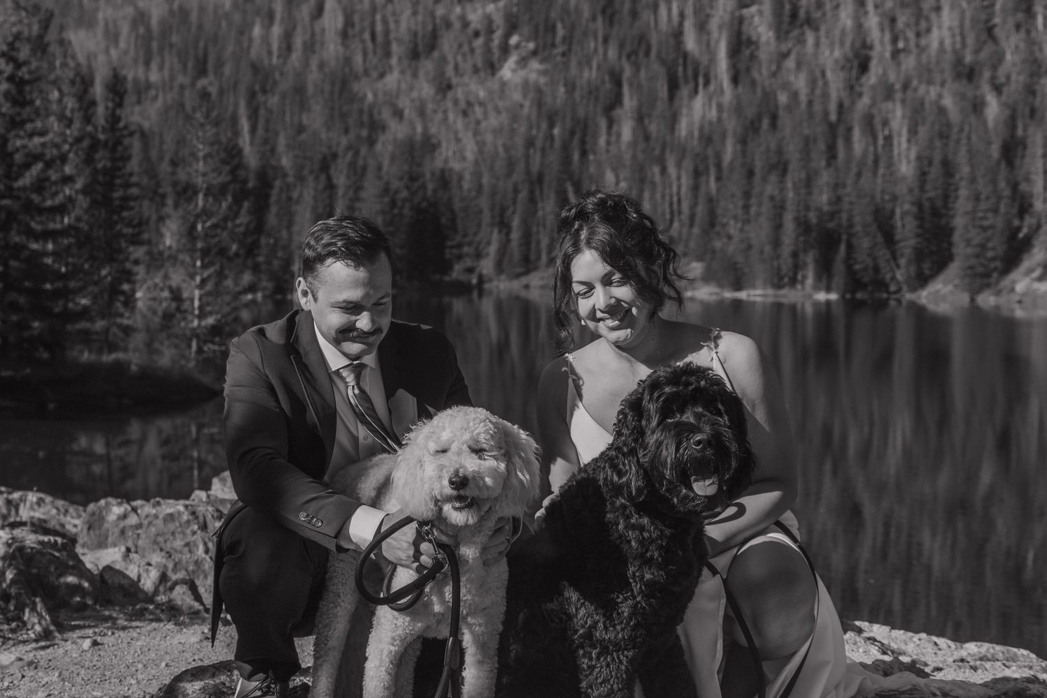 Happy couple with their two dogs by mountain lake in black and white photography.