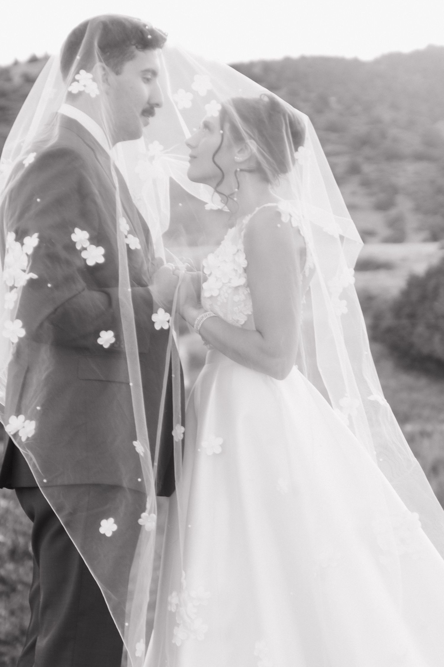 Romantic outdoor wedding scene with flowing veil decorated with delicate white flowers.
