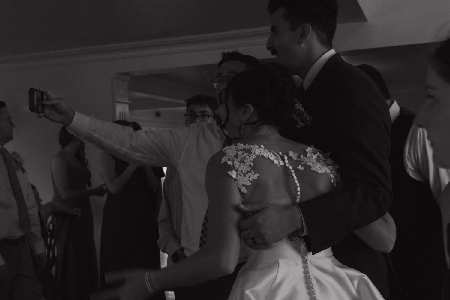 Black and white photo of guests dancing and celebrating at a wedding reception.
