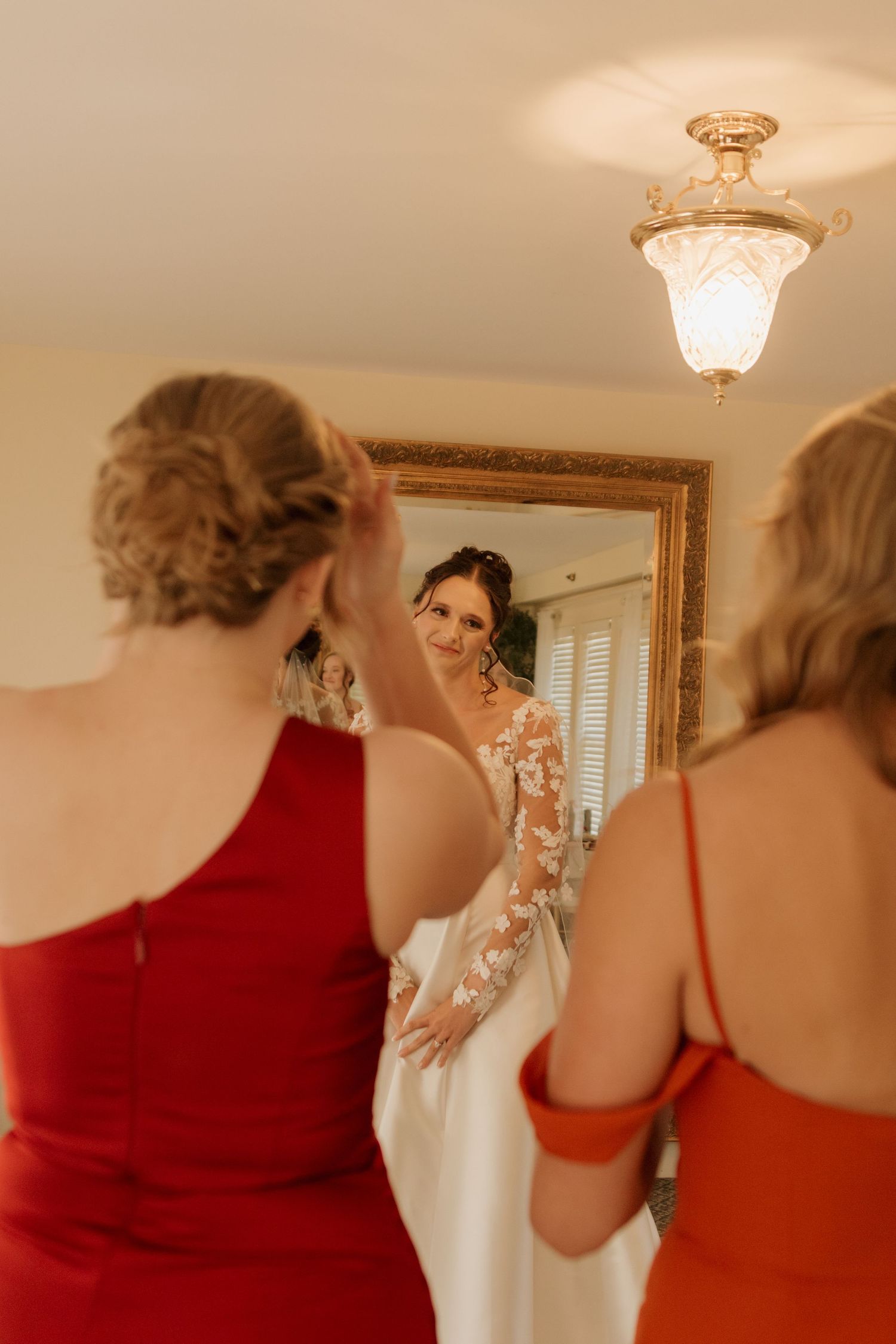 Wedding dress preparations with attendants in red dresses helping with final touches.