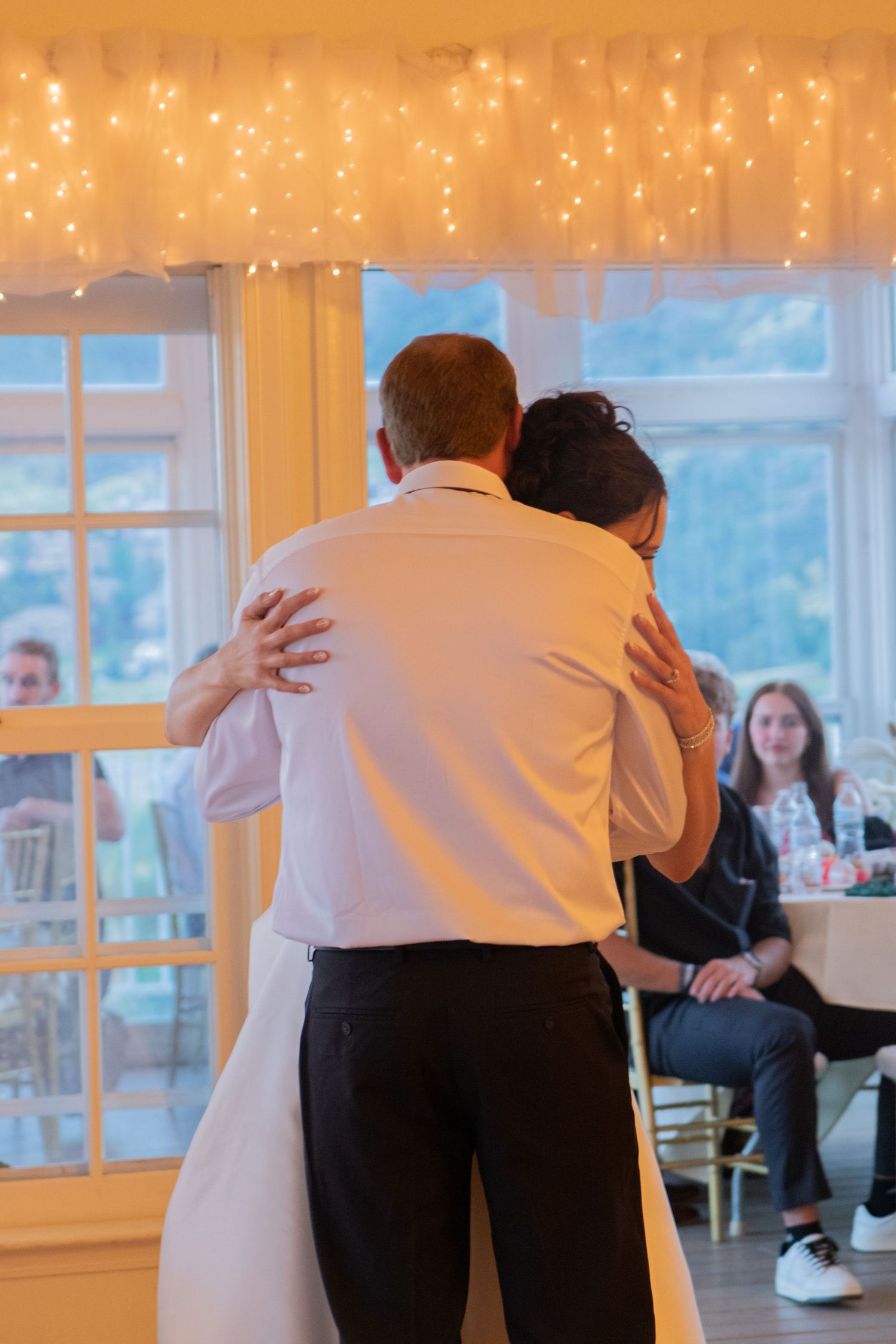 Wedding guests embracing on a dance floor illuminated by string lights.