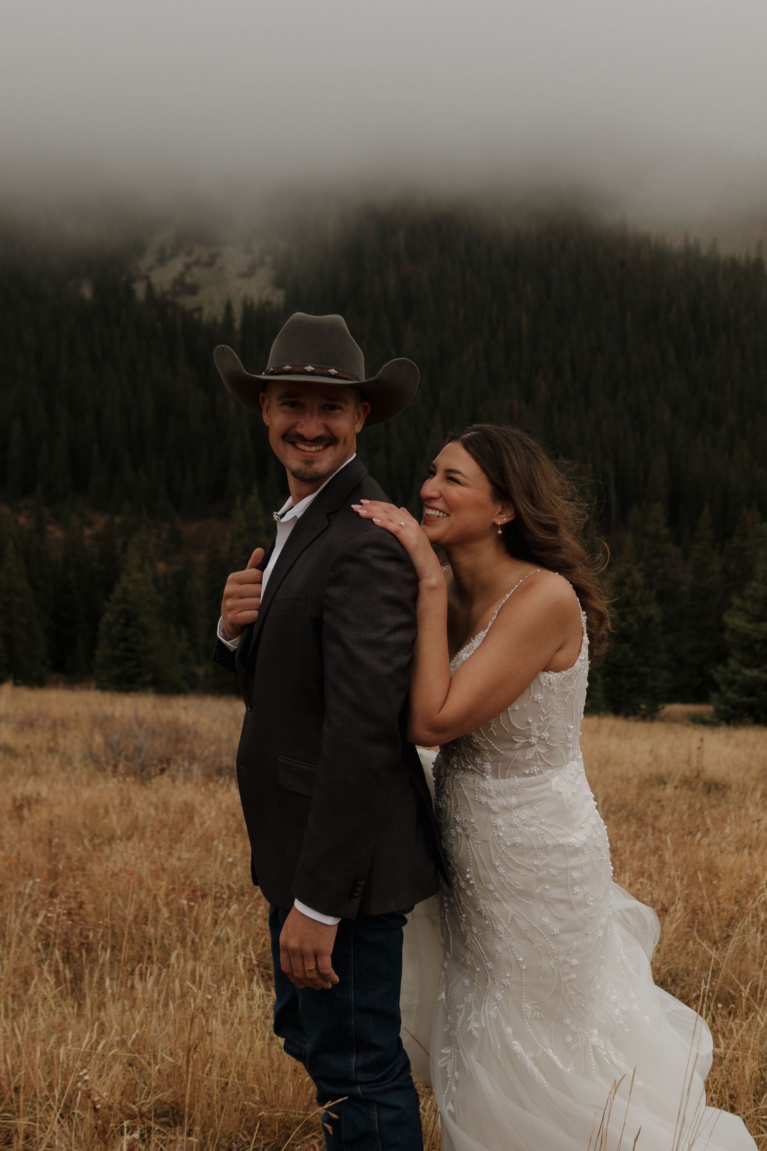 A wedding couple shares a joyful moment in a mountain meadow at dusk.