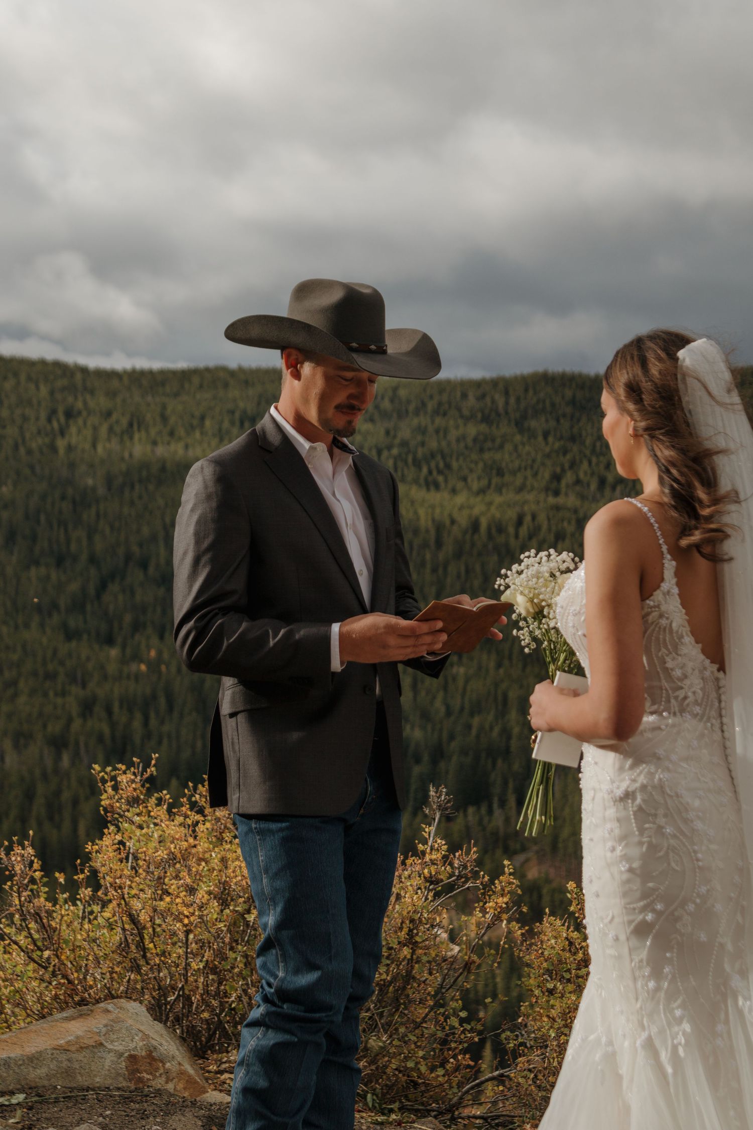 Wedding couple exchanges vows on a mountaintop with evergreen forest in background.