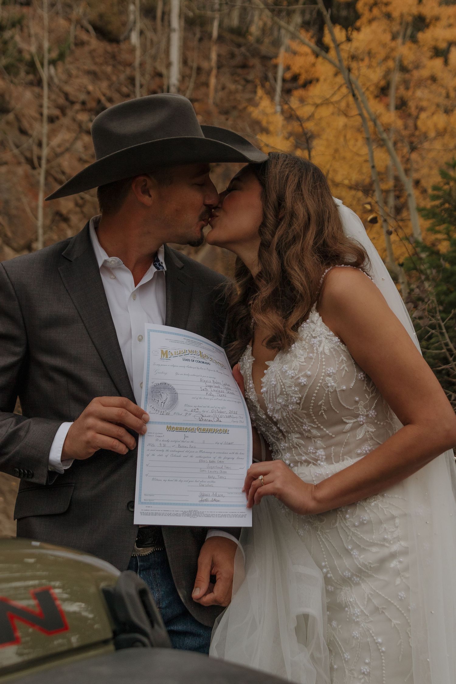 A couple sharing a romantic moment while holding their marriage certificate outdoors.