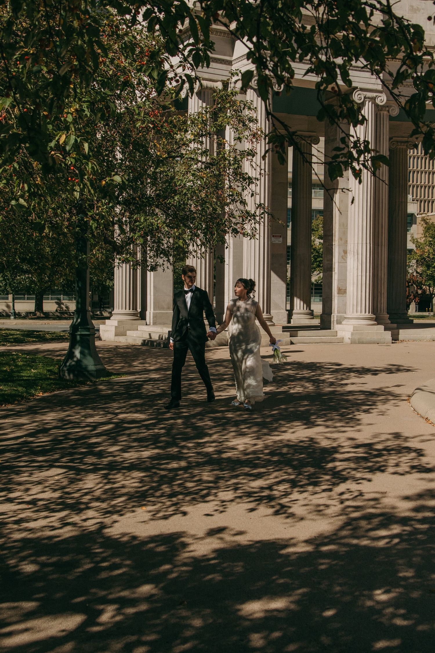 A sunlit colonnade with classical columns casting dramatic shadows on a stone walkway.