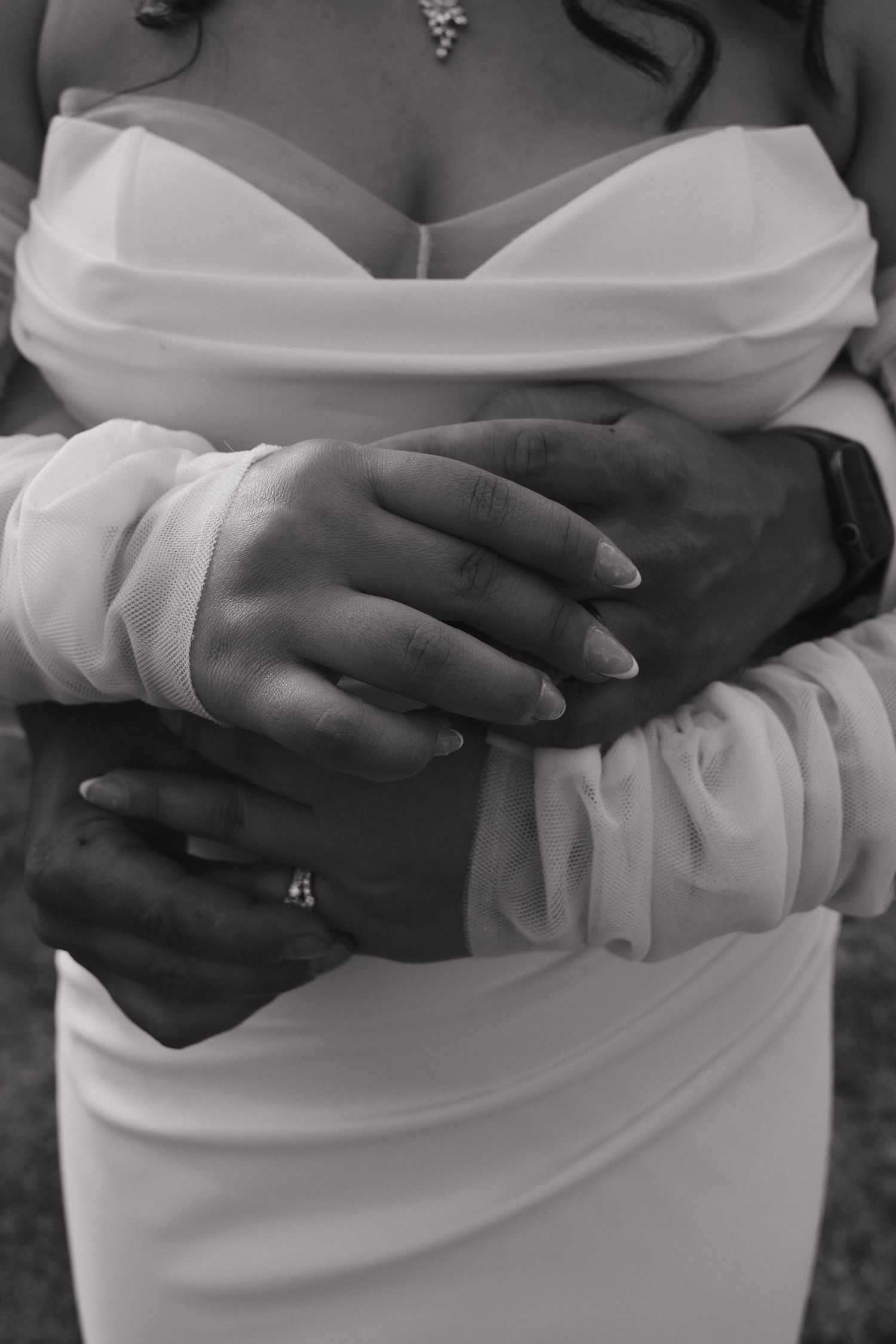 Black and white photo of groom embracing bride in white wedding dress showing rings.