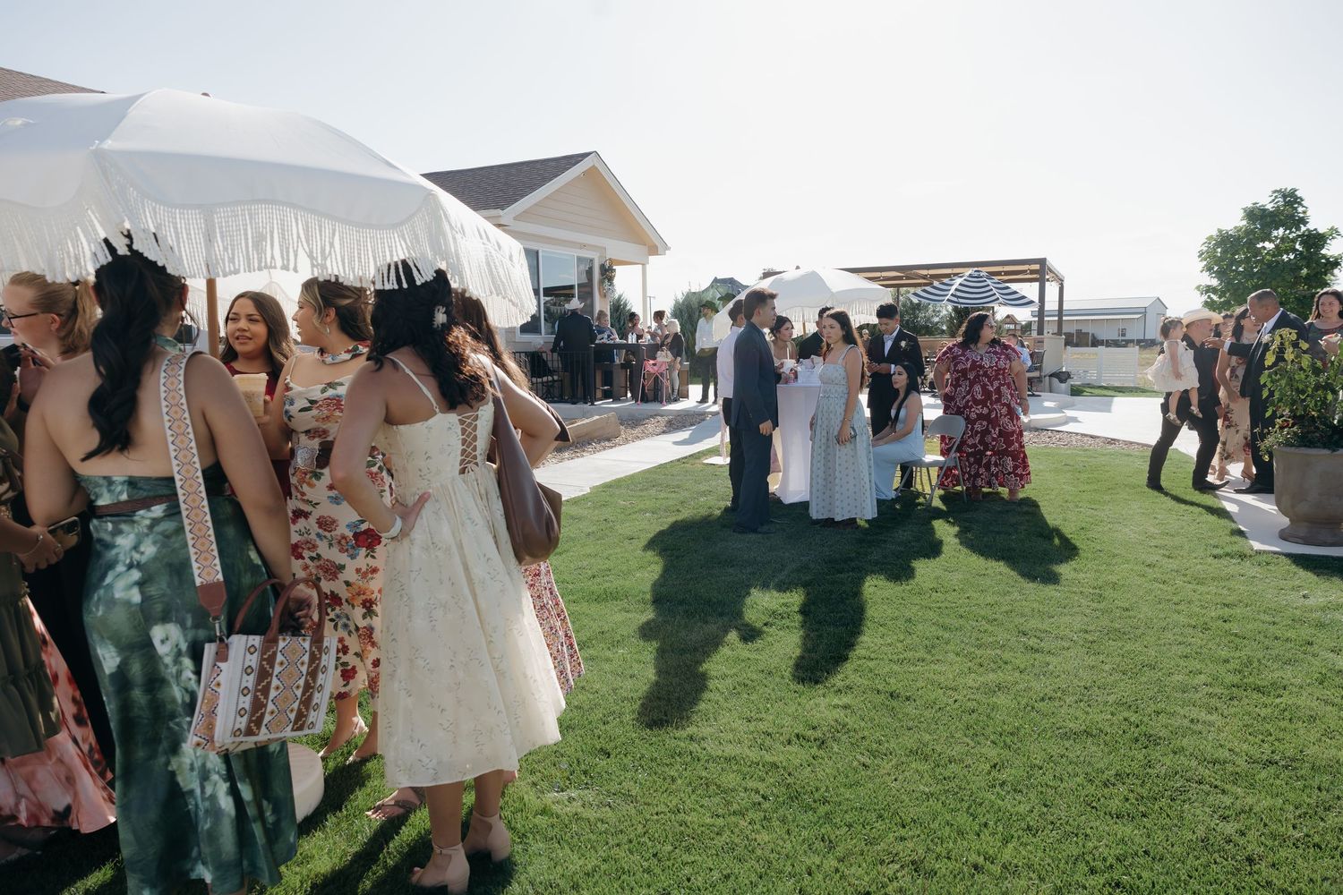Wedding guests mingling on green lawn at outdoor reception venue on sunny day.