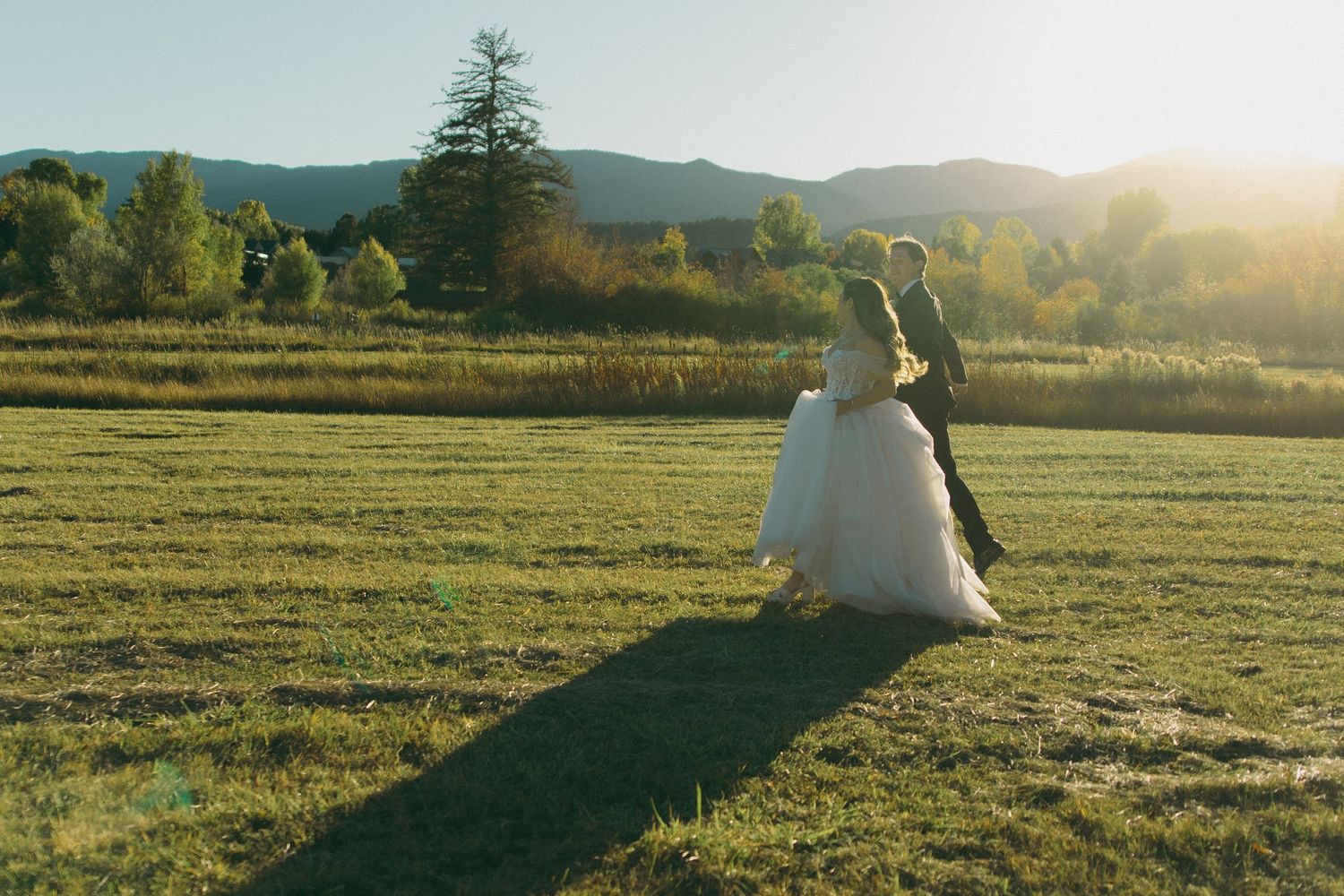 Scenic mountain landscape at sunset with golden light streaming across green meadows and rolling hills.