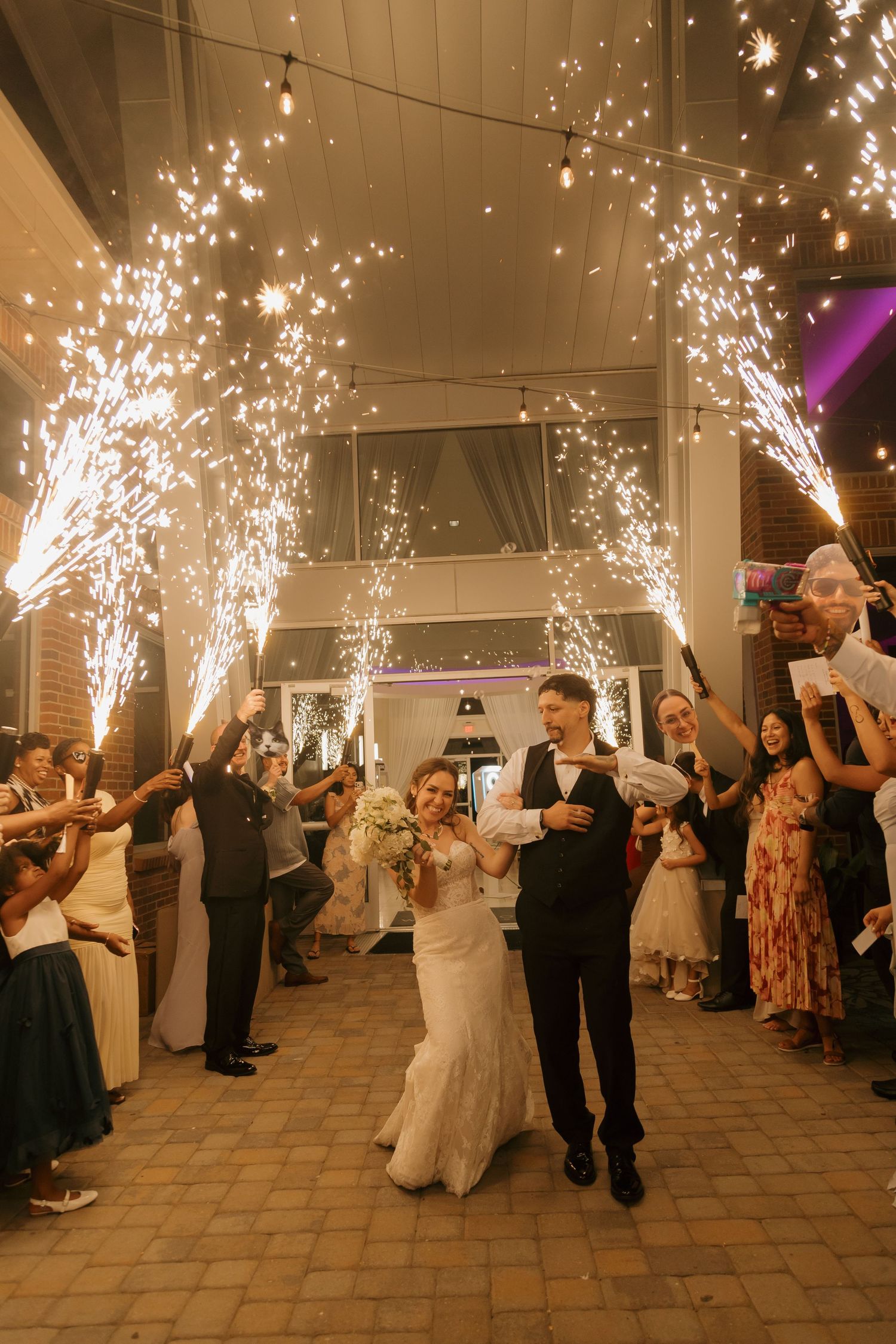 Bride and groom exit wedding reception through dramatic cold sparkler tunnel with guests.