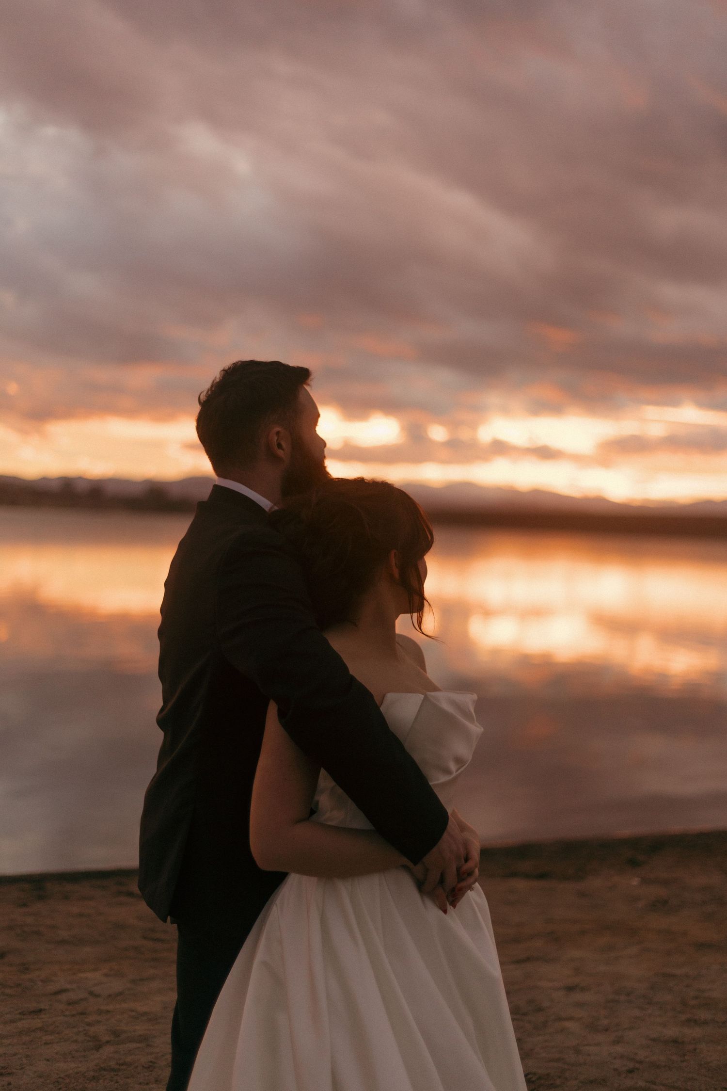 Silhouetted couple embraces against a dramatic sunset sky on their wedding day.
