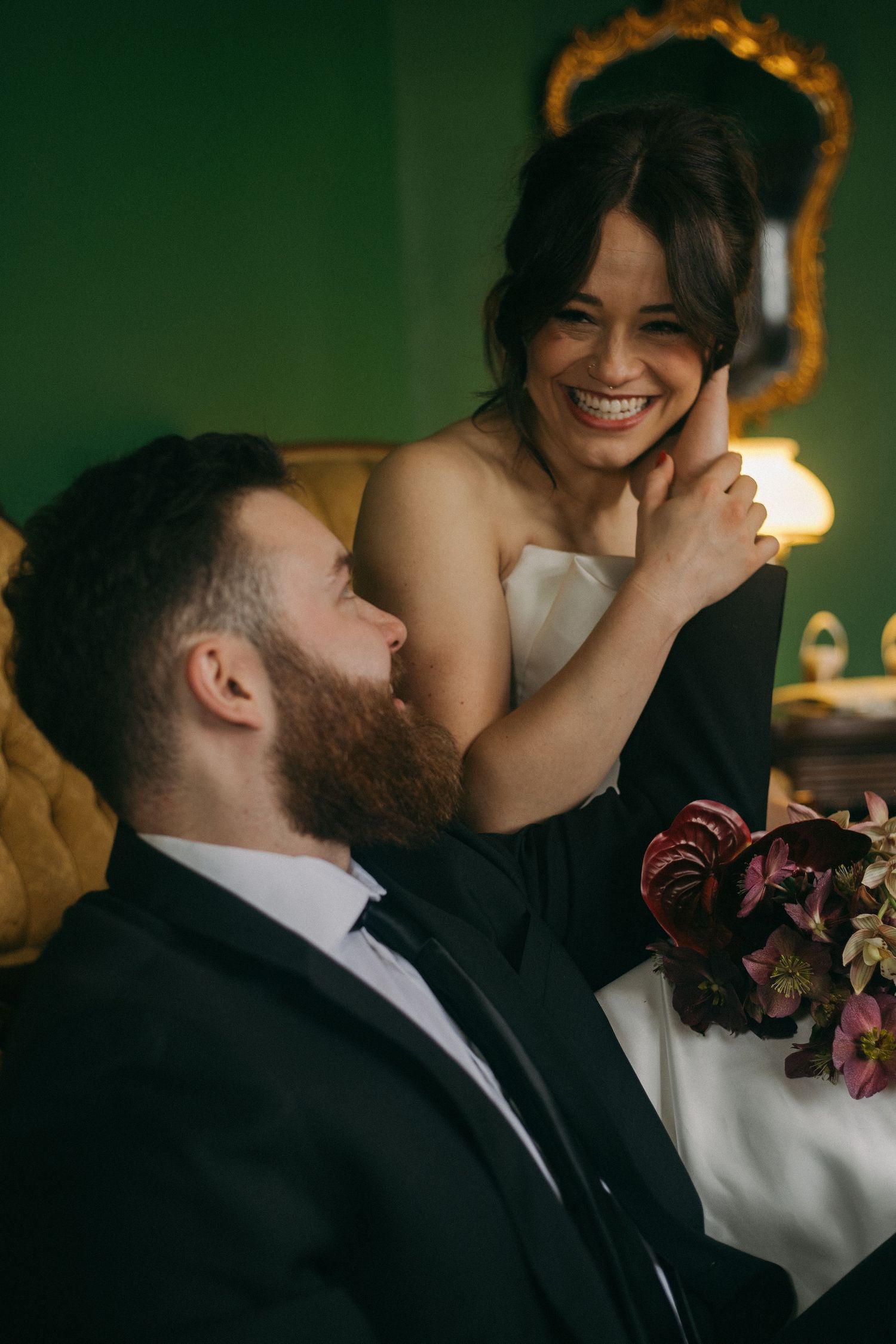 Candid wedding moment captured in warm lighting against emerald green wall.