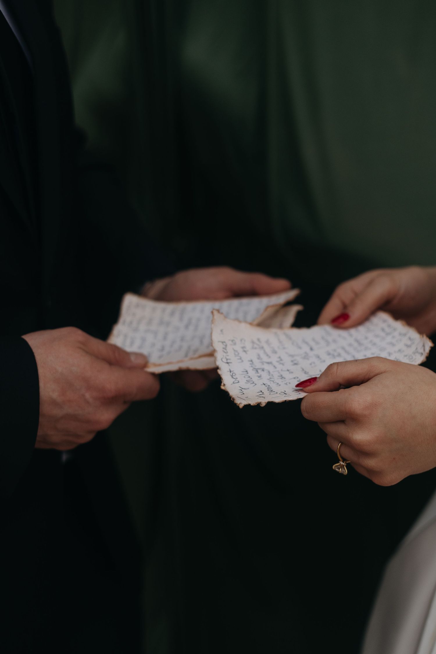 Two hands exchanging handwritten letters or notes against a dark background.