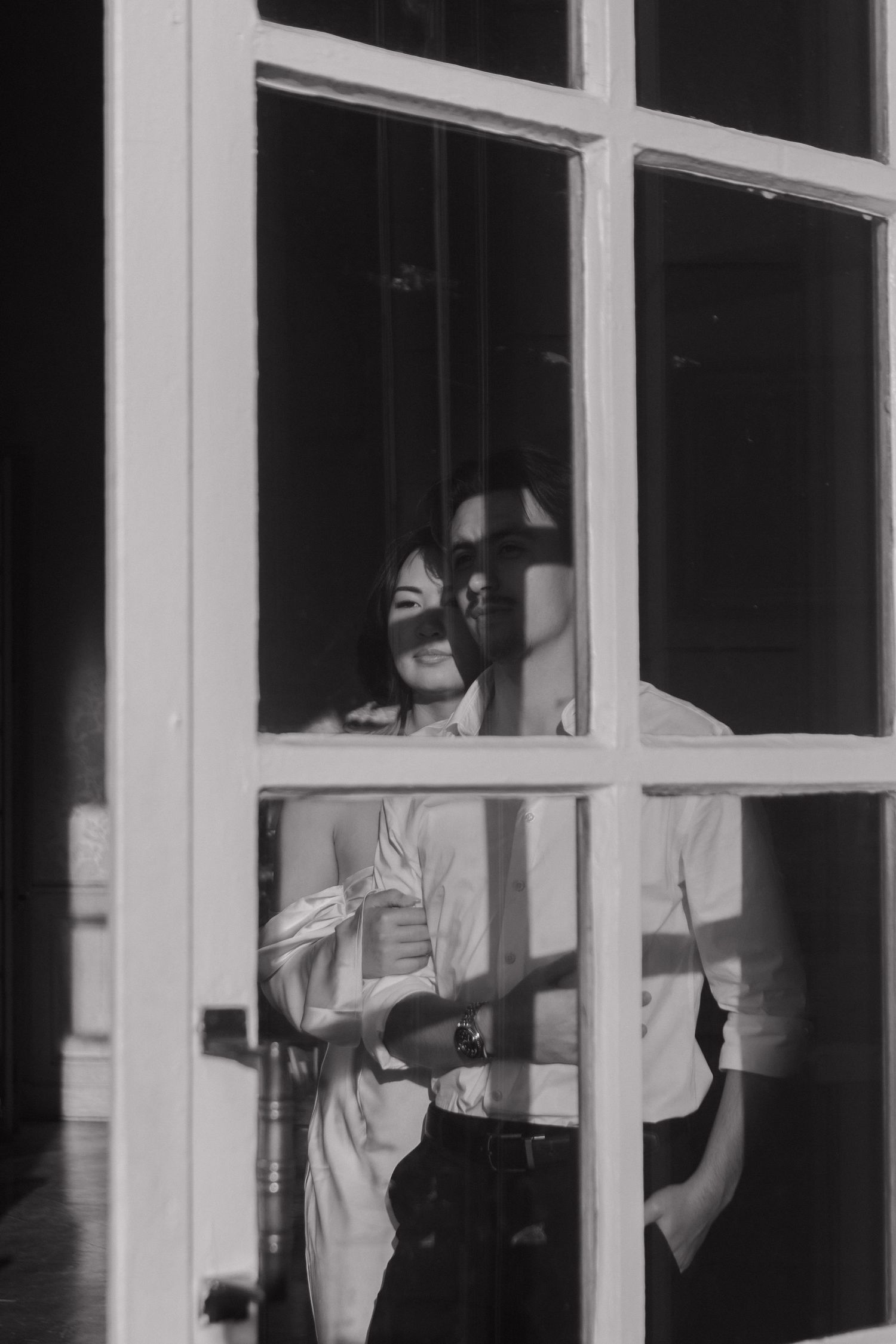 An artistic black and white photo showing a person through window panes, creating a geometric composition.