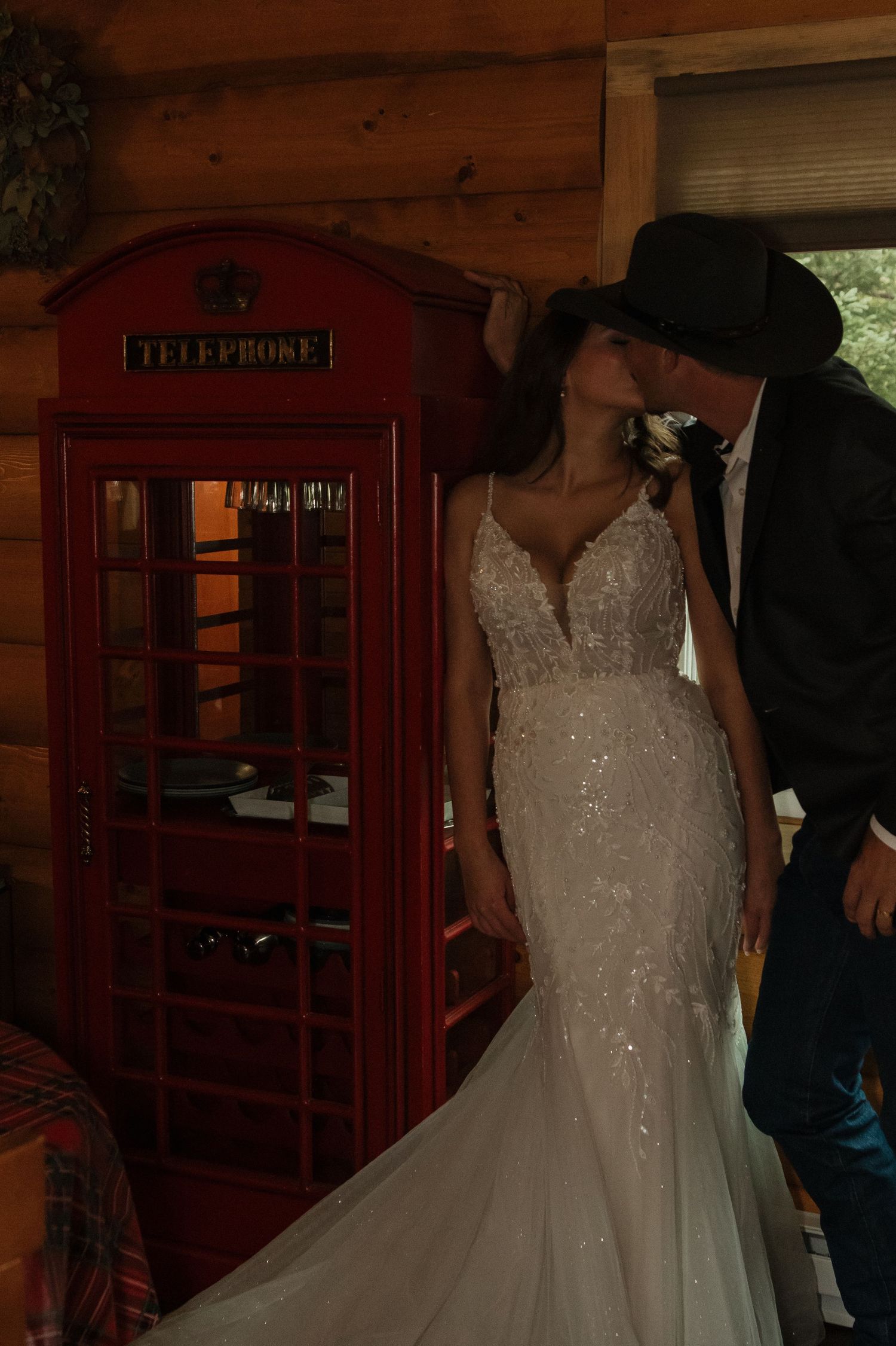 Wedding dress displayed near a red vintage telephone booth in a rustic wooden interior.