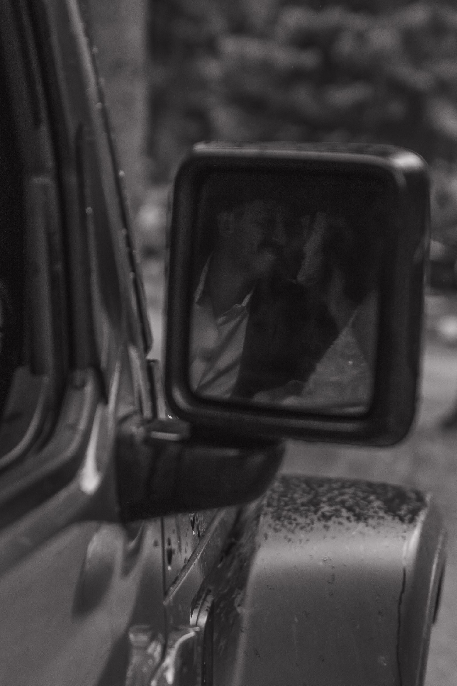 A black and white reflection in a car side mirror captures a wedding moment.